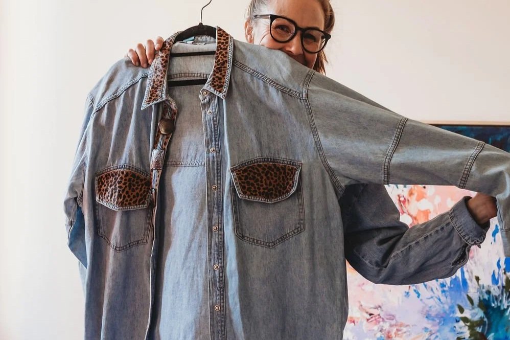 Woman holding up a denim shirt with leopard print accents on collar and pockets.