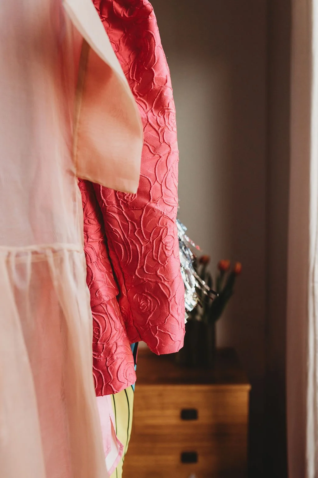 Close-up of pink and peach fabric hanging on a closet rod with a flower vase in the background.