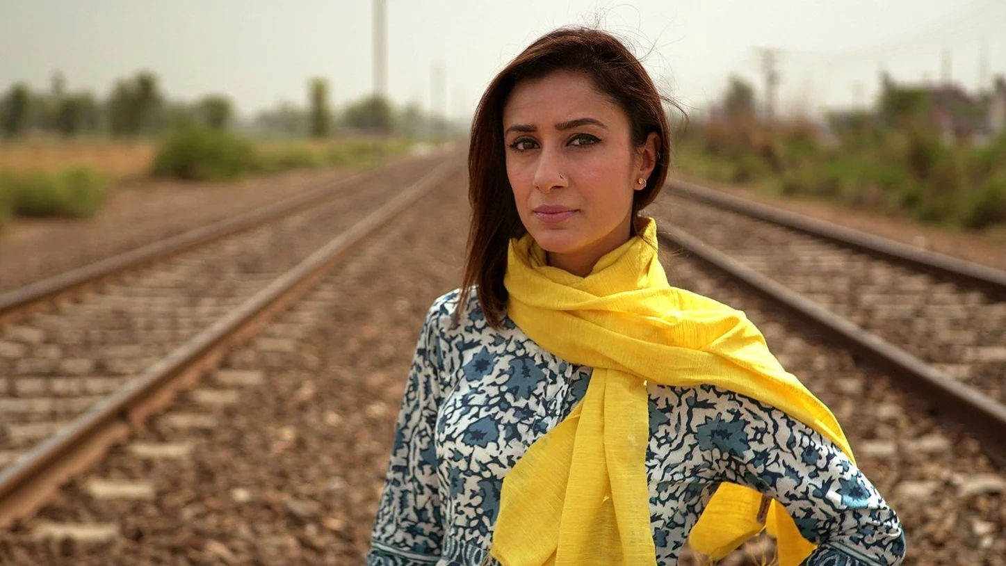 Anita Rani in a yellow scarf on railroad tracks