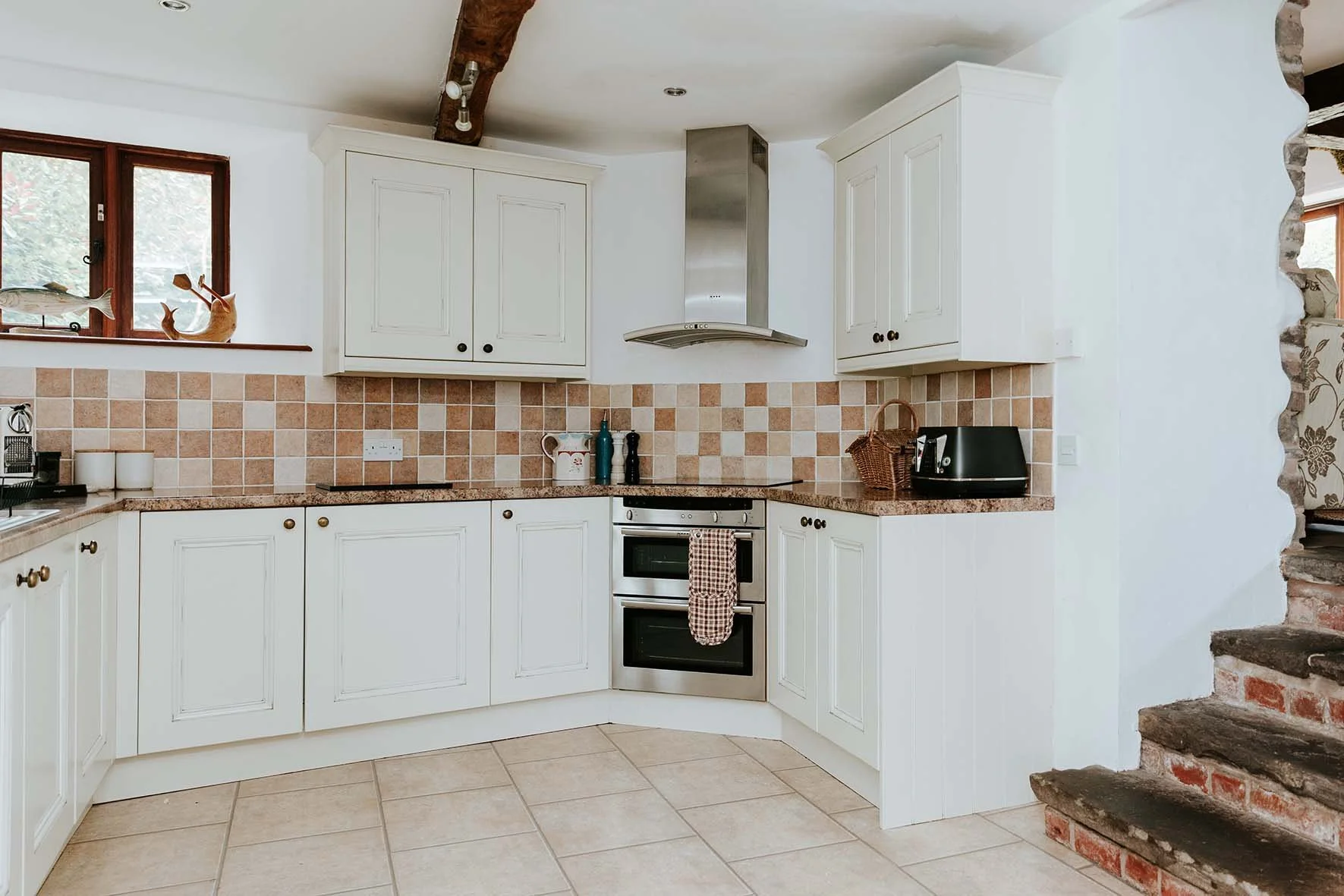 Kitchen with white cabinets, beige tile backsplash, stainless steel oven, black toaster, and a small window with a fish and whale decorative piece on the windowsill.