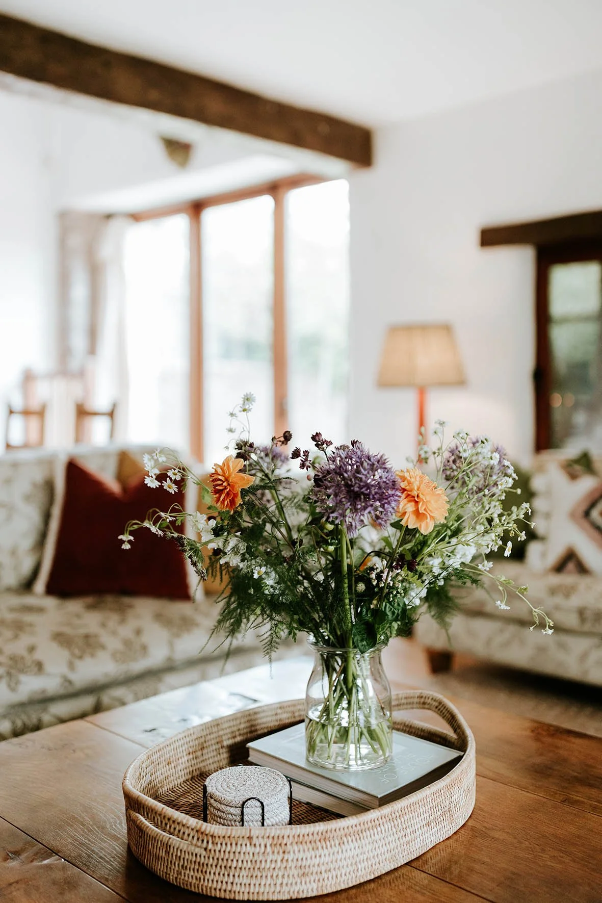 A glass vase with a colorful bouquet of flowers on a wooden table in a cozy living room.