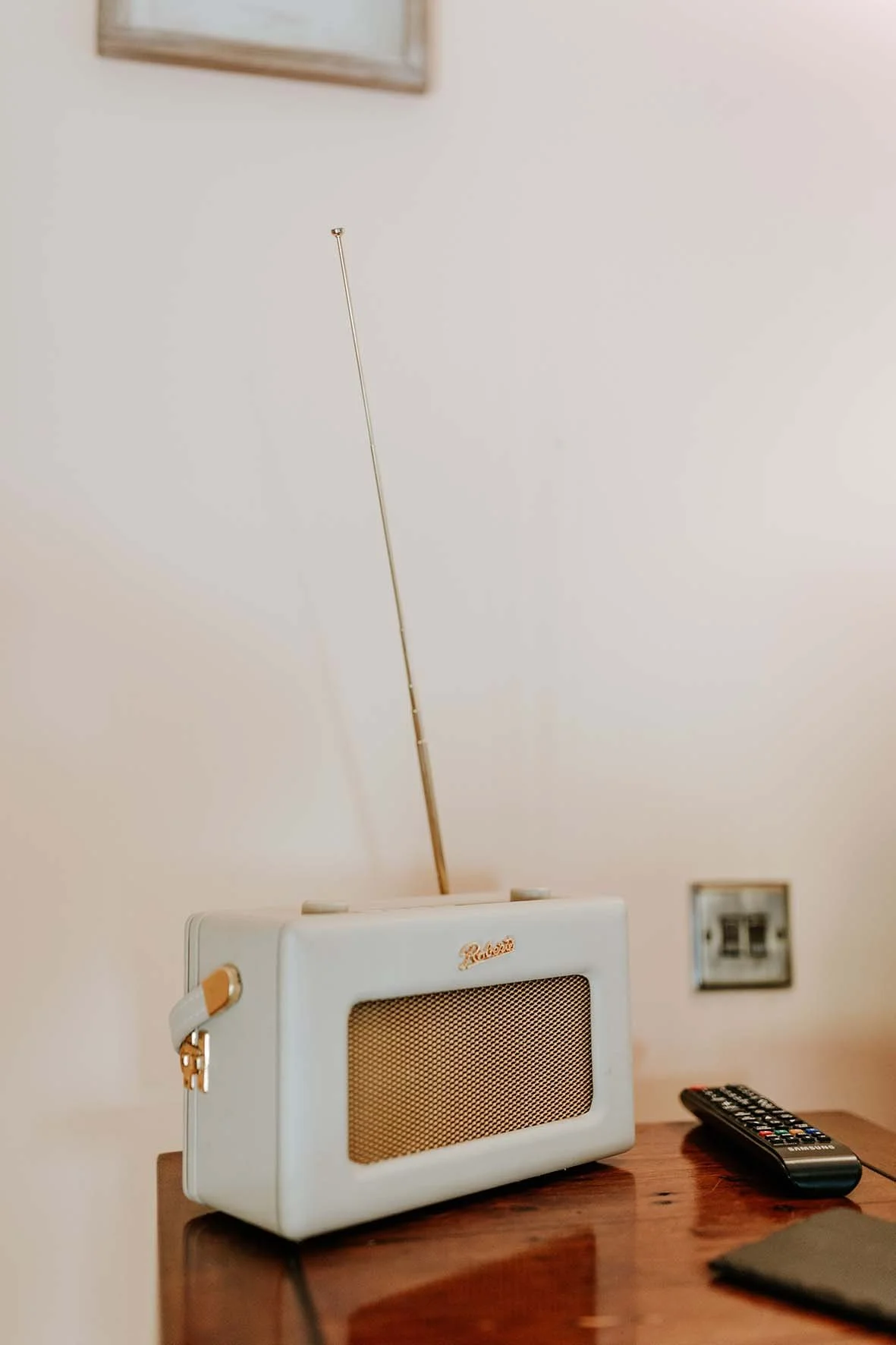A vintage radio with a gold antenna on a wooden table, with a TV remote and a closed notebook nearby.