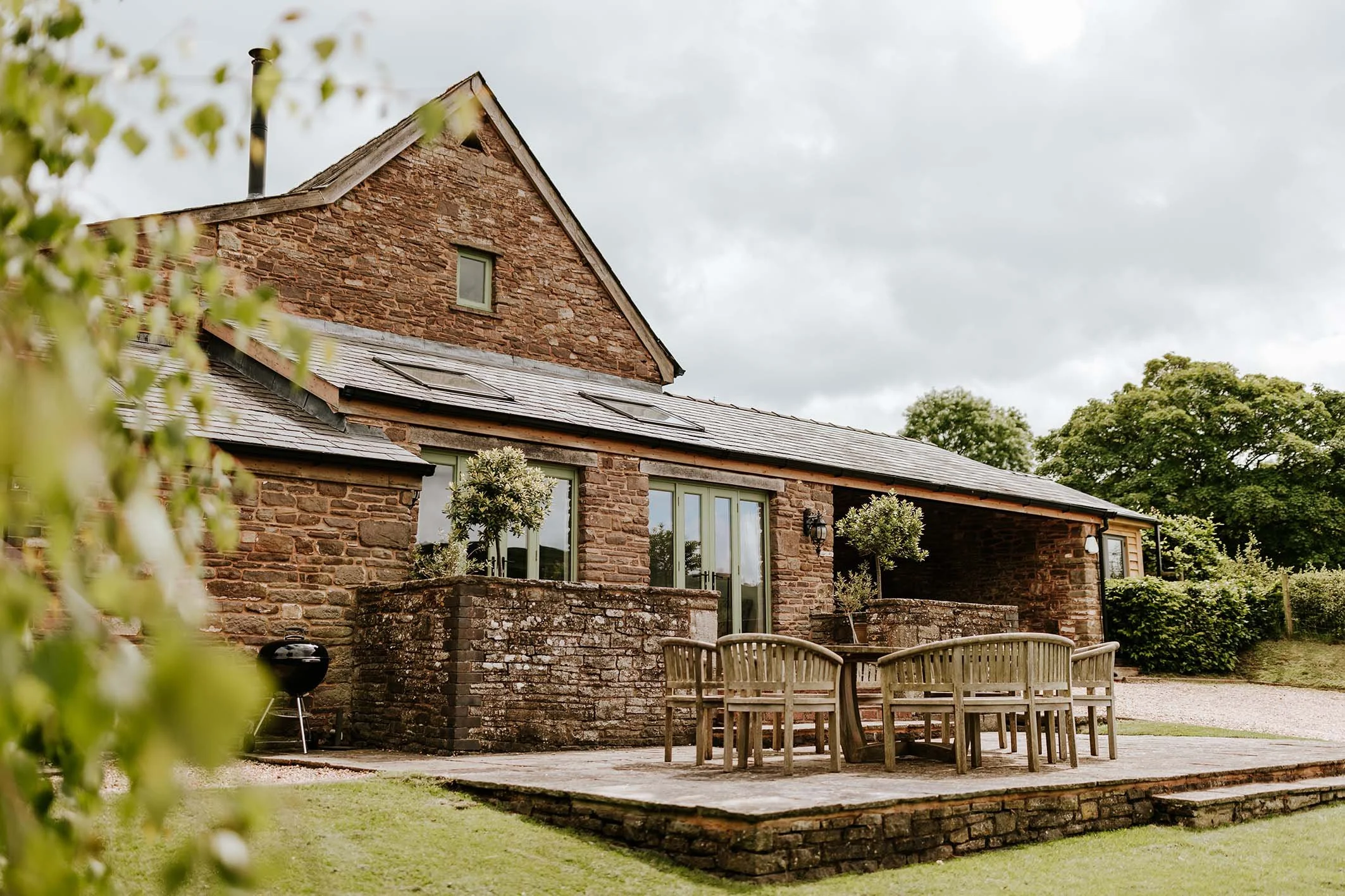 Brick house with slate roof, glass double doors, and outdoor patio with wooden table and chairs.