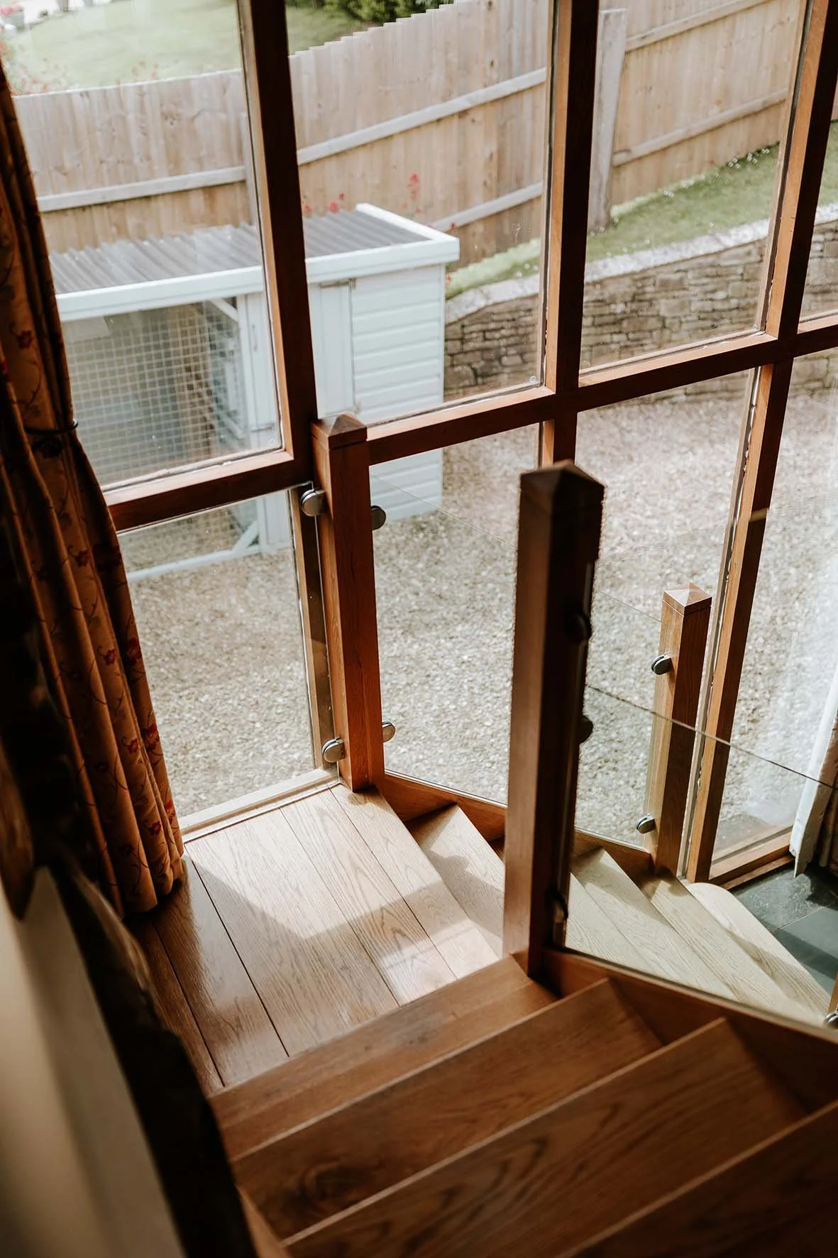 View from a staircase looking out through a glass door onto a gravel yard, wooden fence, and a small white shed outside.