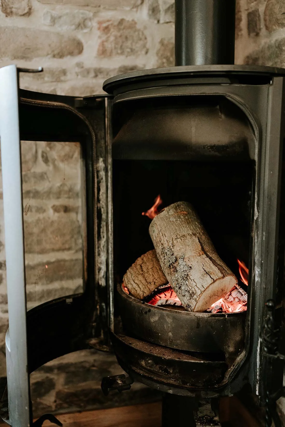A wood-burning stove with logs inside, surrounded by a stone wall.
