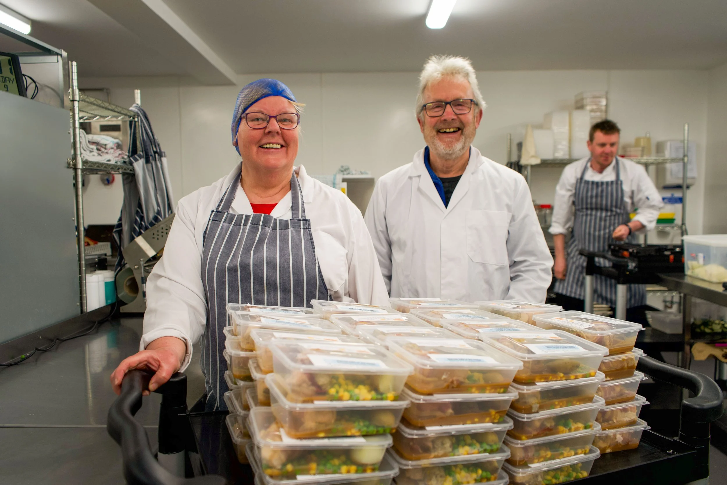 Team members and volunteers smiling in front of a stack of packaged meals at the Giraffe Community Kitchen in Perth
