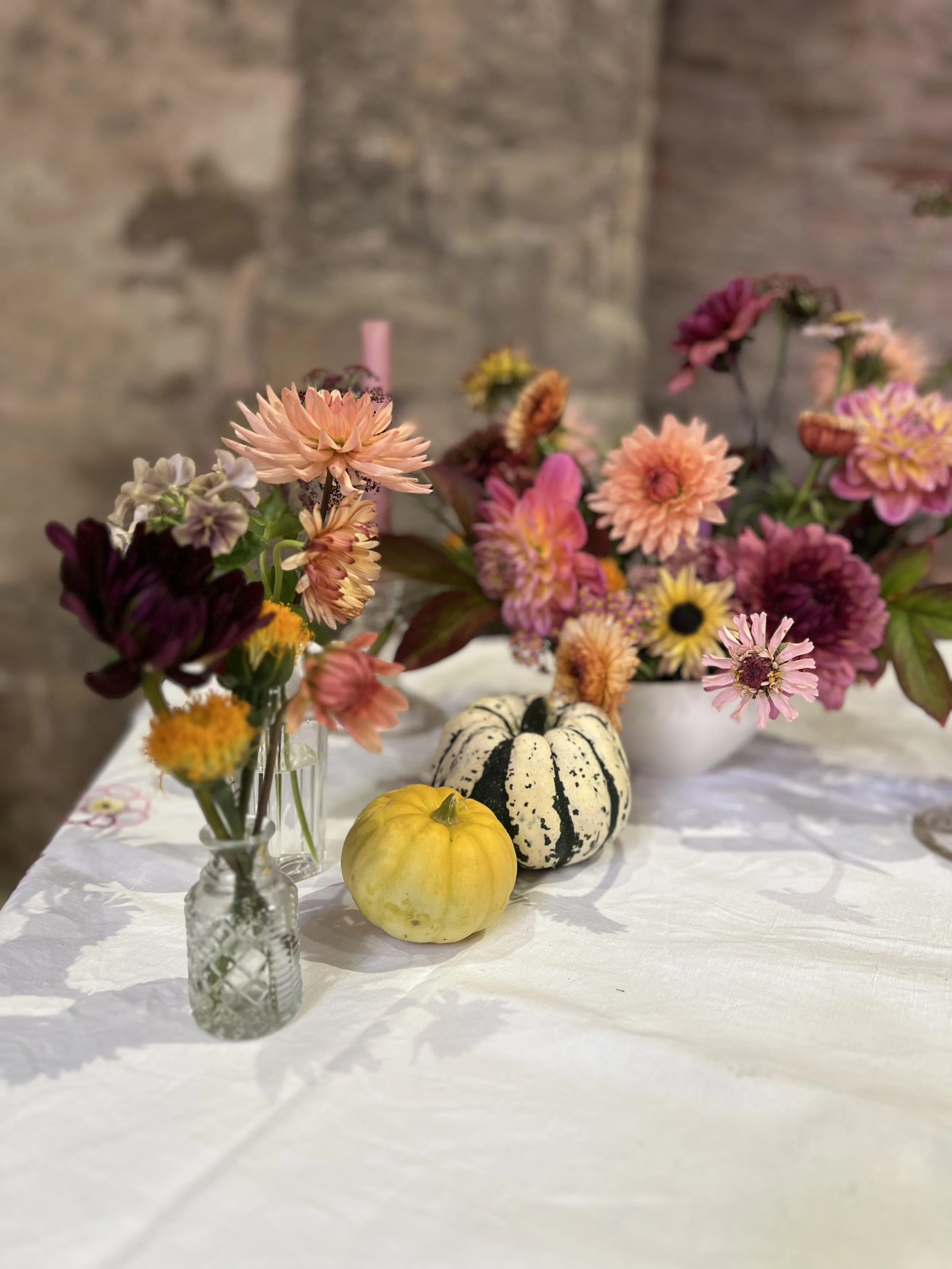 An autumn table scape, bud vases with pink, orange and red dahlias interspersed with small gourds and pumpkins