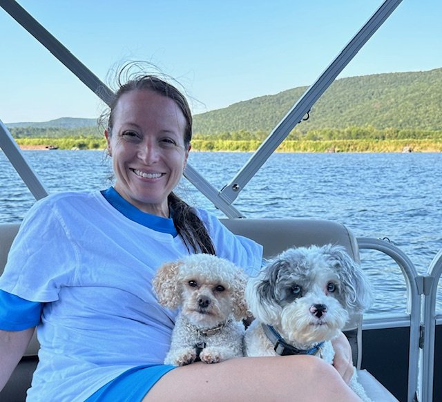 Jenny Wiggins, ALC, smiling with her two dogs on a boating adventure