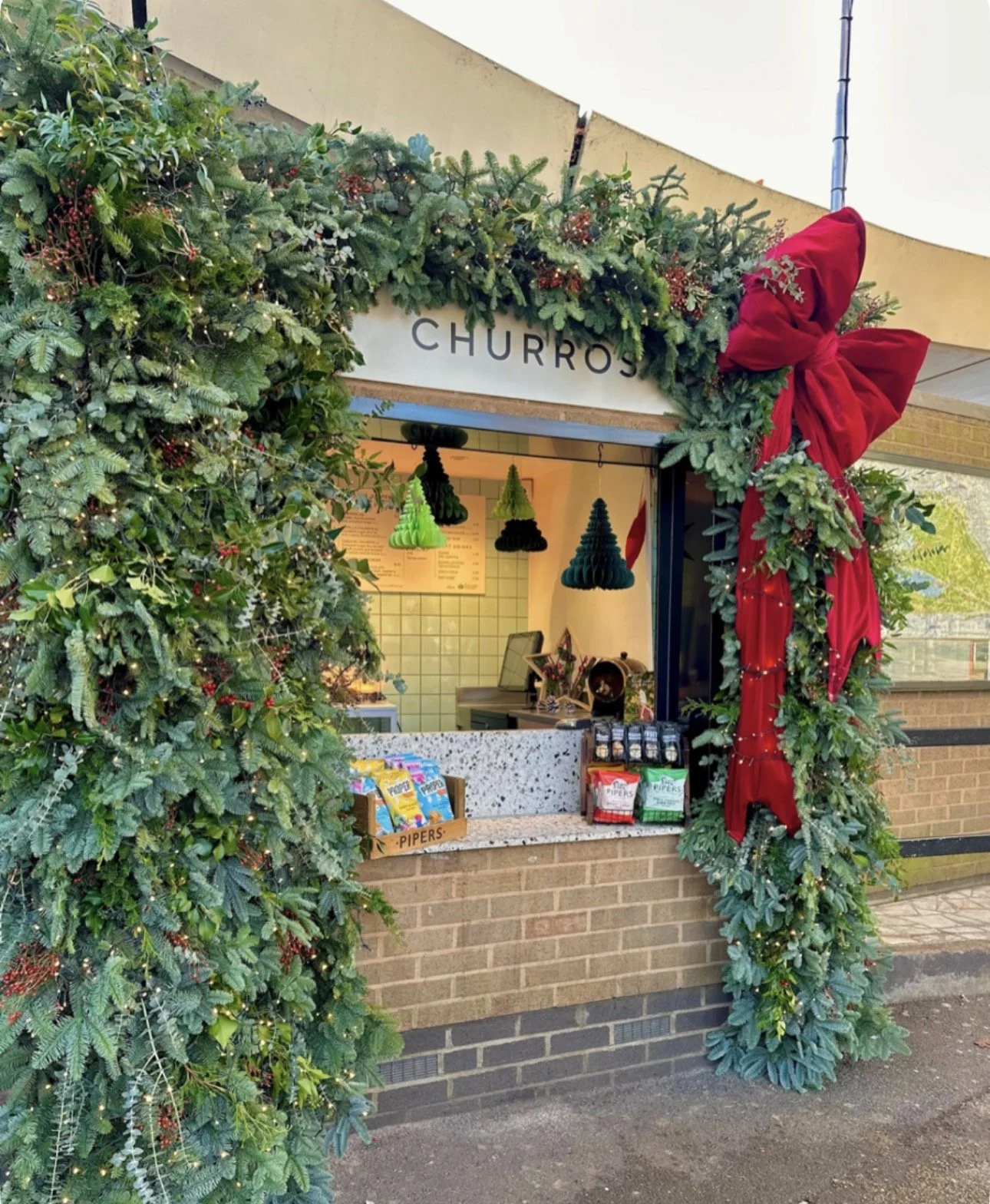 Holiday decorated churro stand with Christmas greenery and a large red bow.