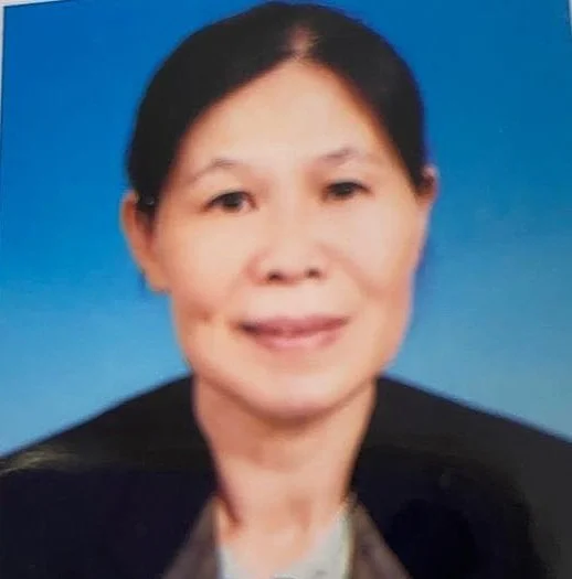 A portrait of a middle-aged woman with dark hair, smiling, wearing a dark blazer against a blue background.