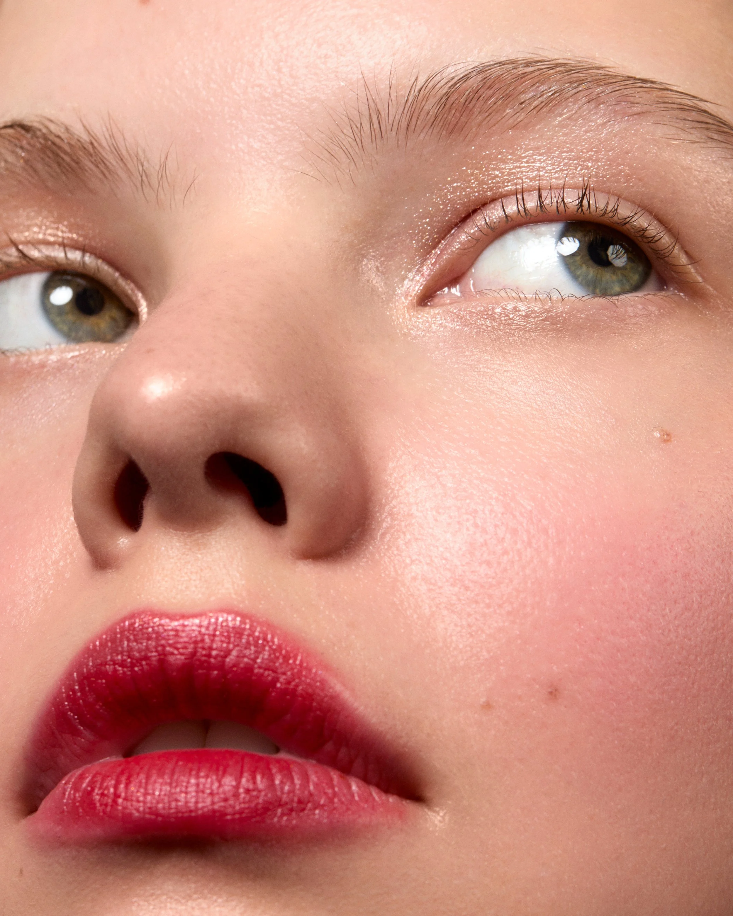 Close-up d'une femme avec peau claire, yeux verts, maquillage léger, lèvres rouges, et sourcils fins.