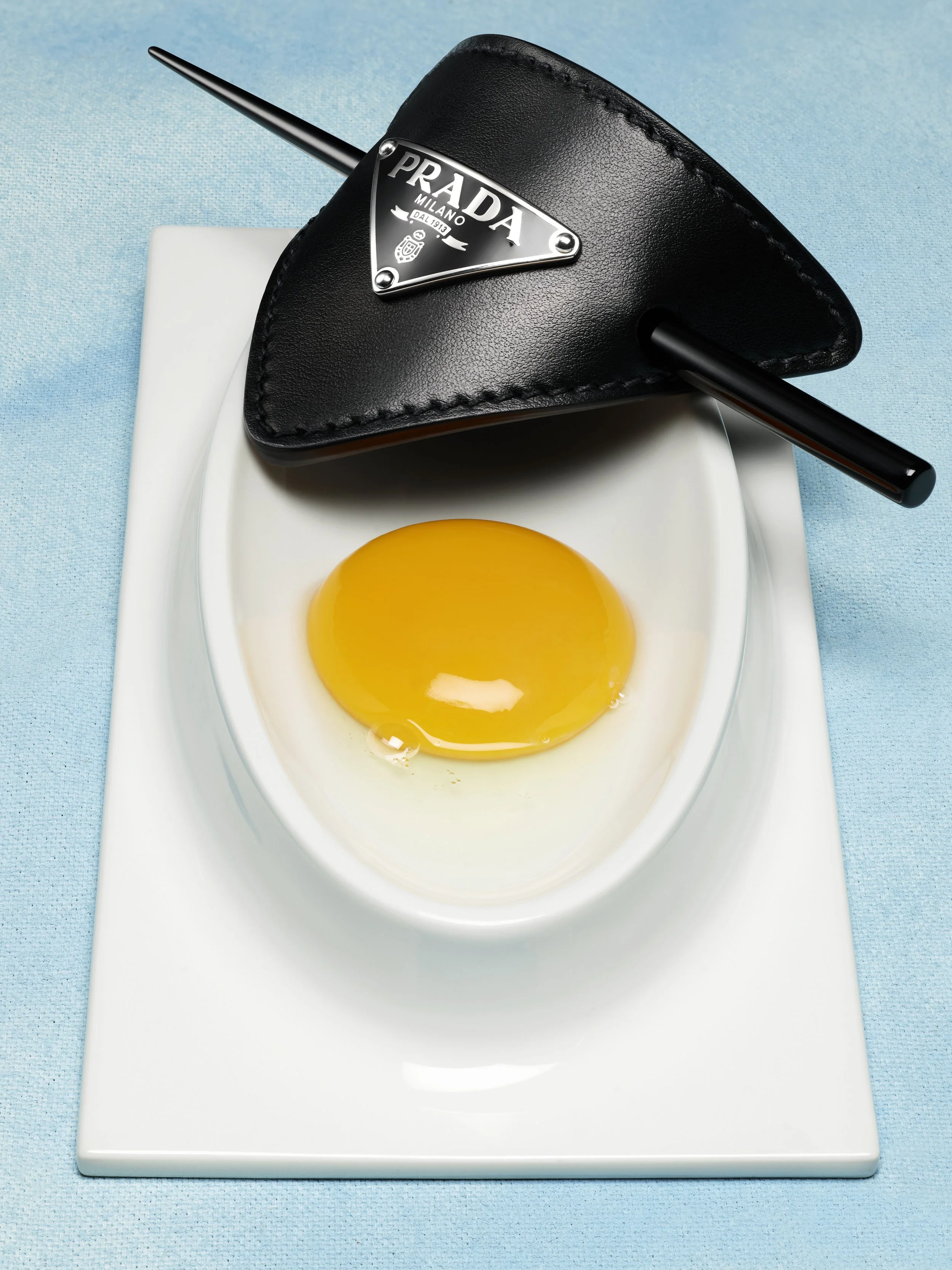 Œuf cru dans une assiette blanche, voit un porte-monnaie en forme de casquette avec une paille en métal.