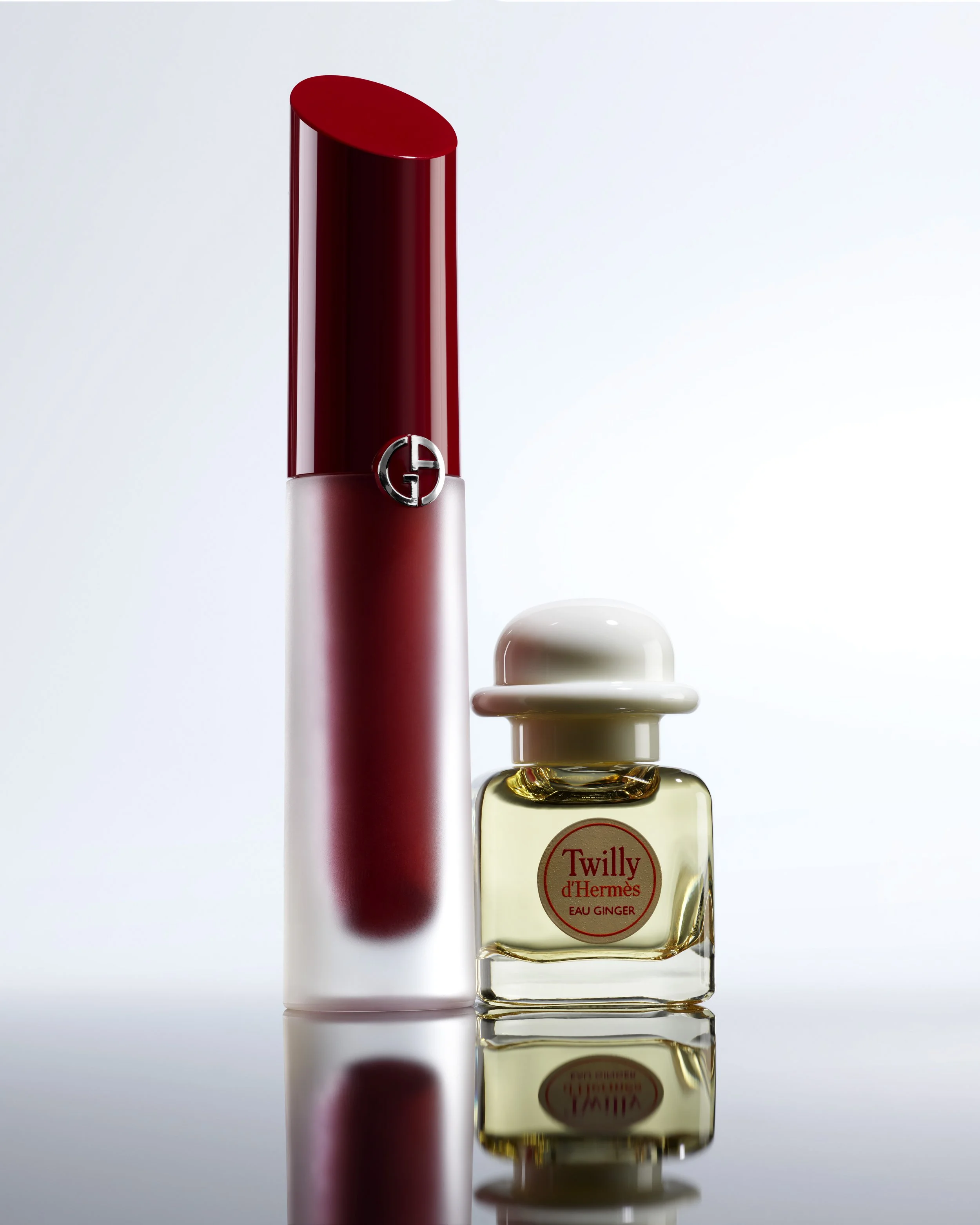 Deux flacons de parfum, un rouge de la marque Giorgio Armani et un de couleur transparente avec un bouchon blanc, étiqueté 'Twilly d'Hermès Eau Ginger'.