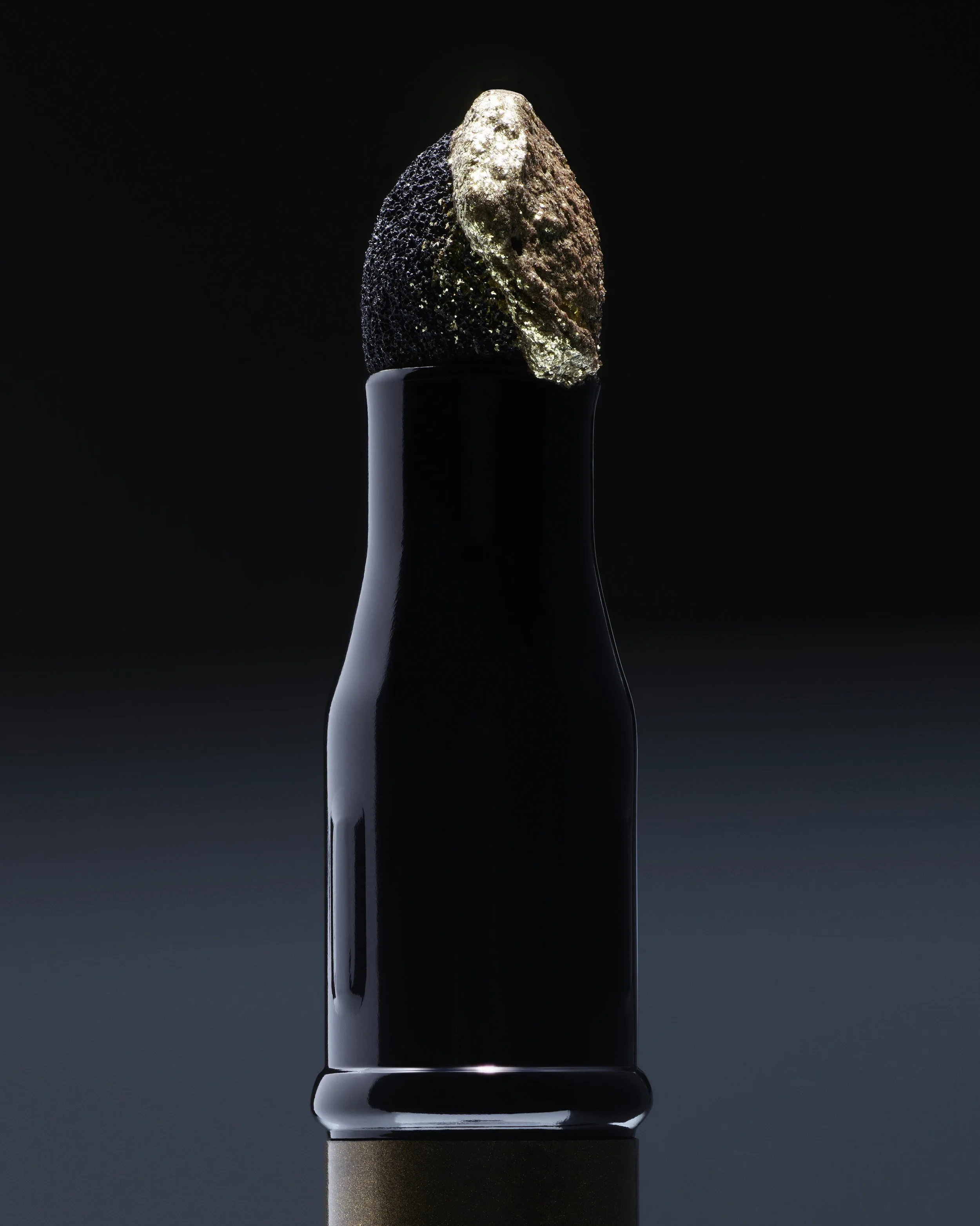 Une bouteille noire contenant probablement du liquide, avec un bouchon recouvert de poudre d'or et de caviar noir.