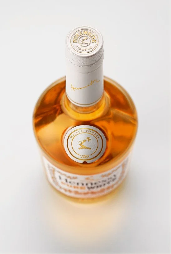 Bouteille de cognac avec étiquette blanche et logo doré, vue du dessus.