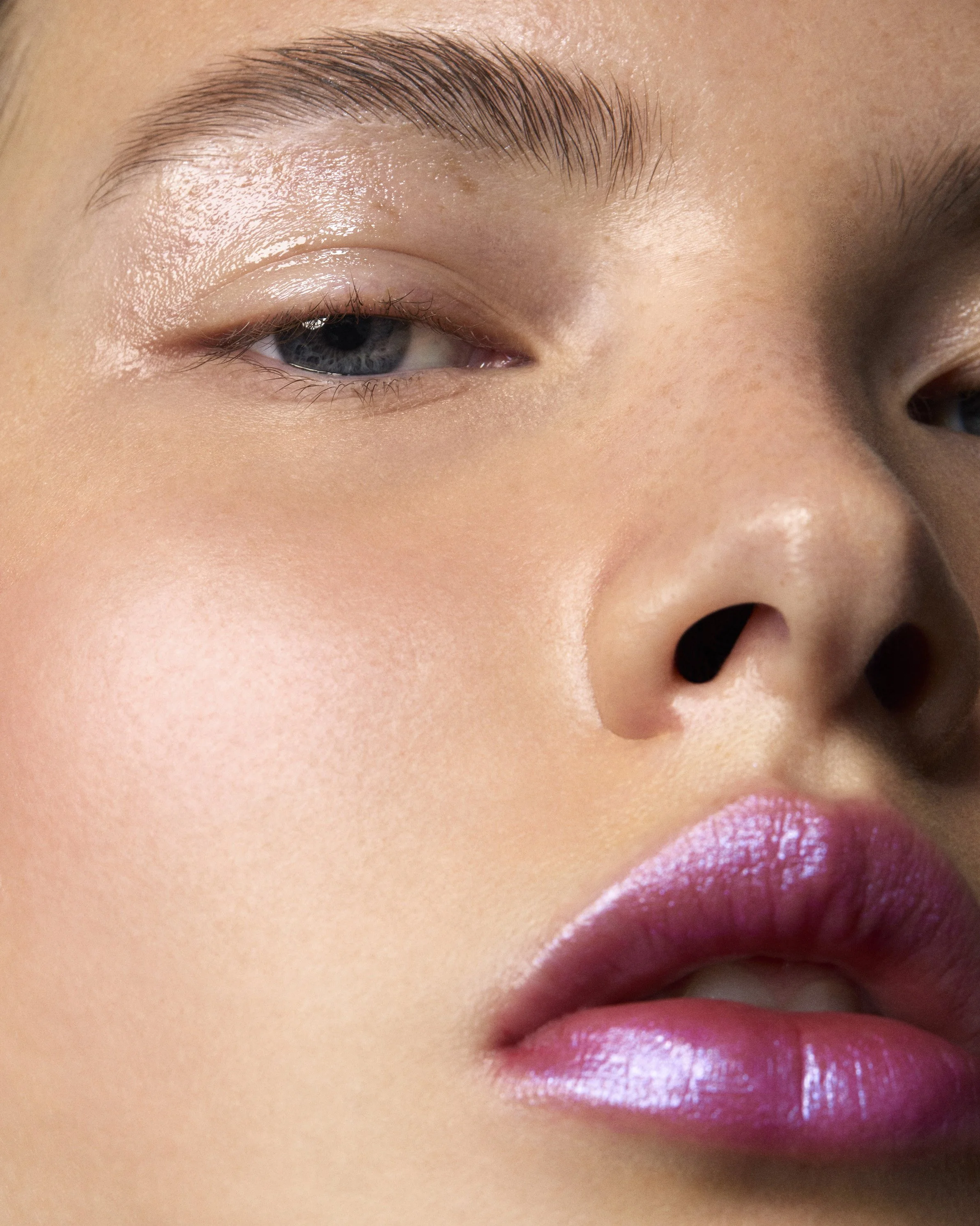 Gros plan d'une personne avec une peau impeccable, lèvres glossy, et un œil semi-clos.