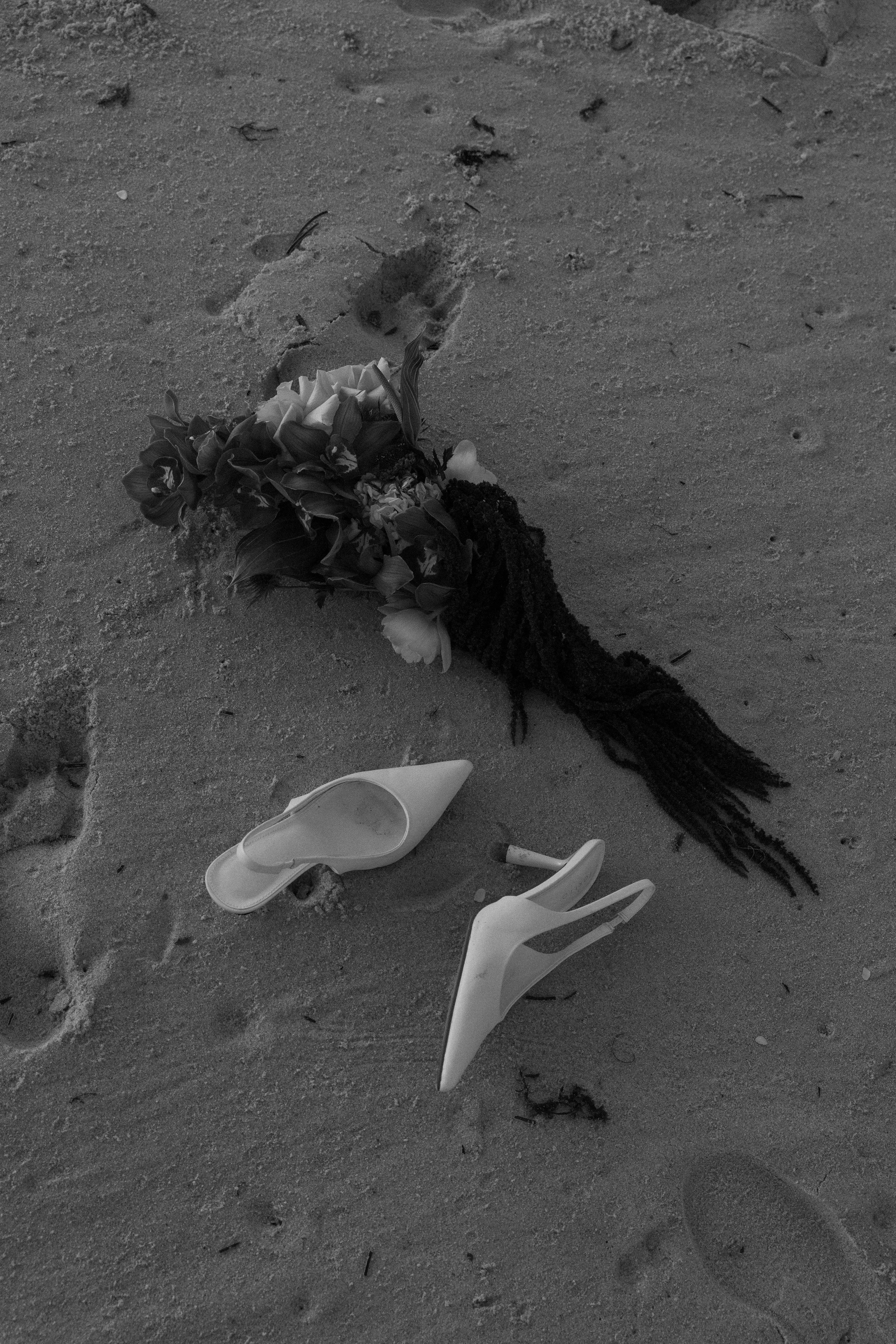 A bouquet of flowers and a pair of high-heeled shoes on sandy ground.