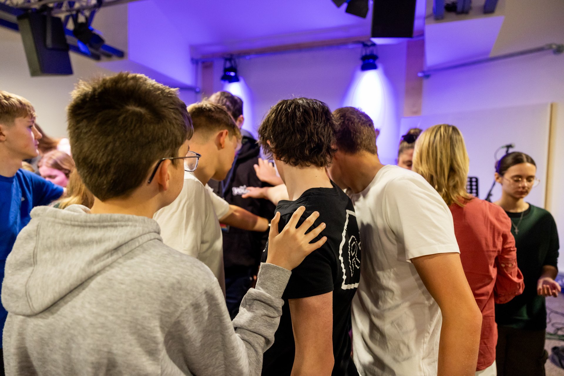 Group of teenagers embracing in a circle in a room with purple and white lighting.
