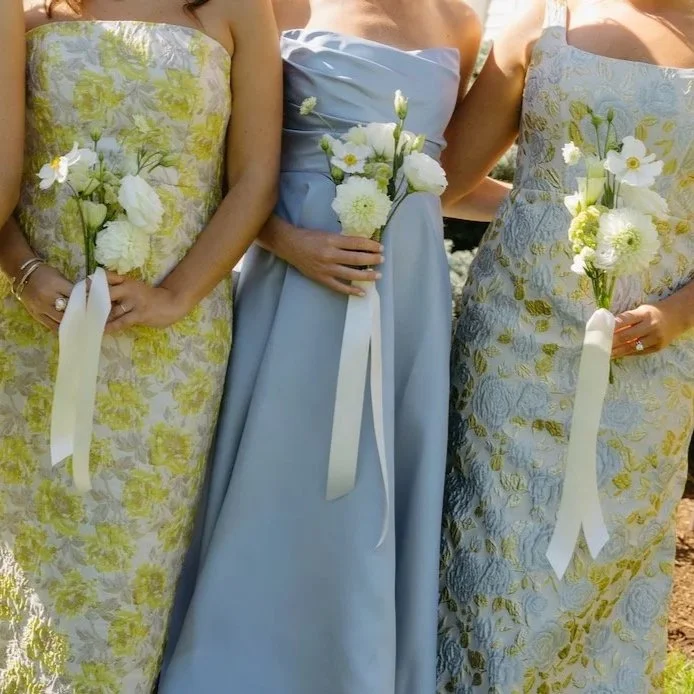 Close-up of three women in elegant dresses, holding petite sculptural bridesmaids bouquets.