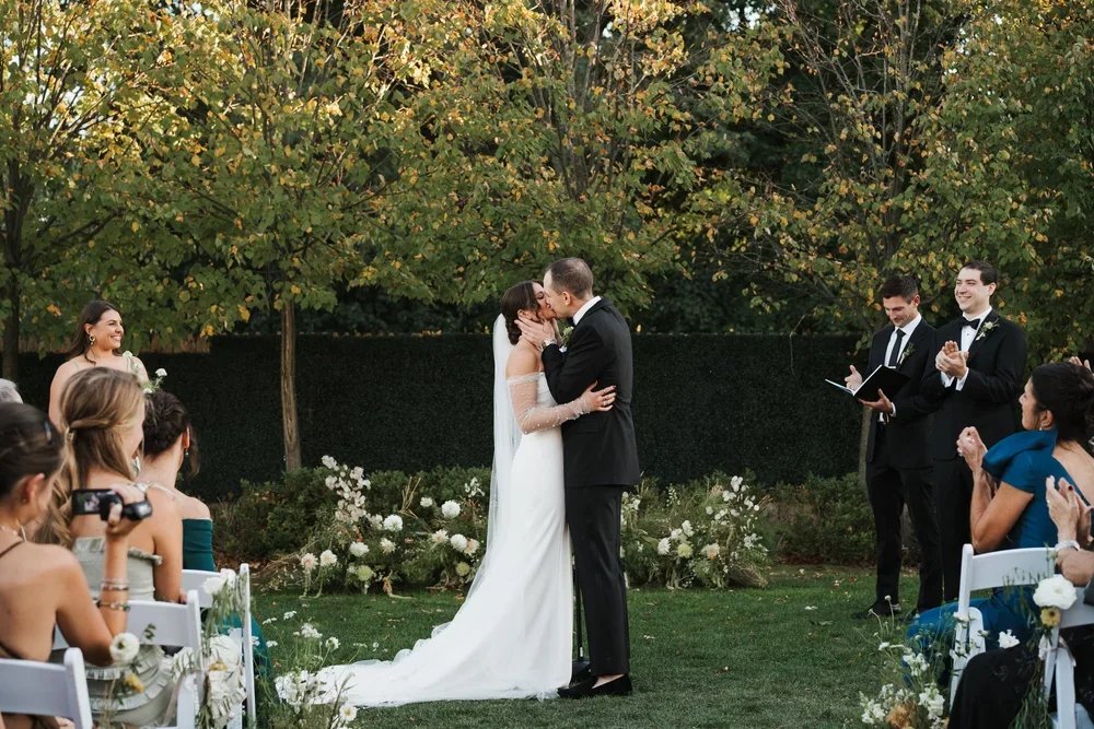 Delamar West Hartford Wedding Photo of meadow-style wedding flower arrangements for ceremony backdrop as the couple kisses