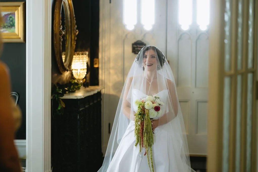 A Bride stands in the foyer of this grand New Haven wedding venue, with a huge smile and her cascading bridal bouquet.