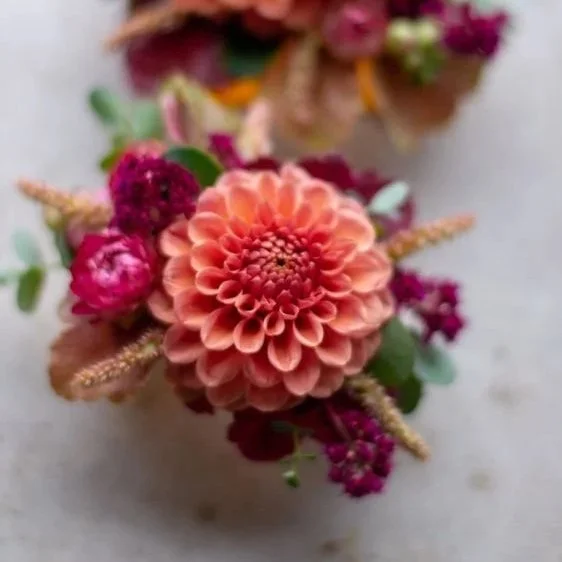 Close-up of a small bouquet with a peach-colored dahlia, pink heather, and other colorful flowers.