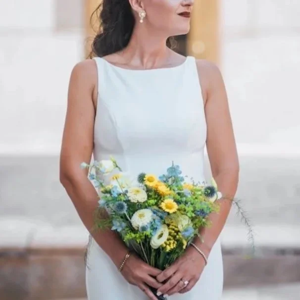 Woman in white dress holding a bouquet of yellow, white, and blue flowers.