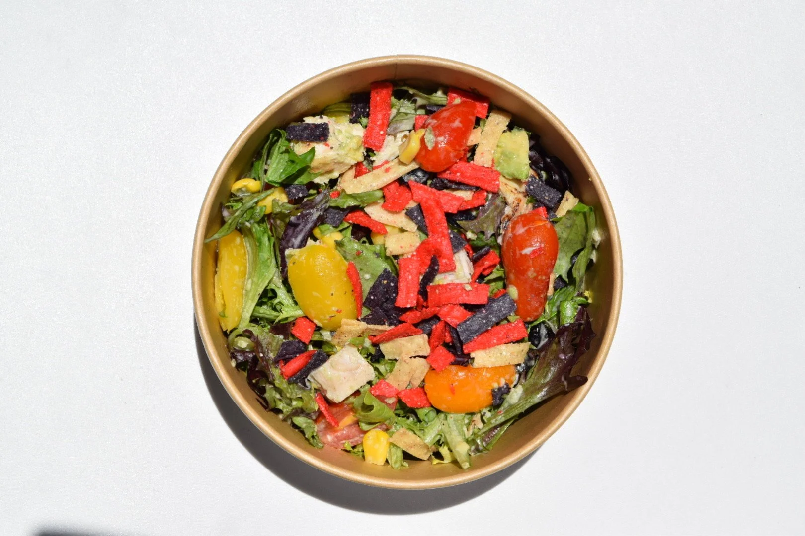 a salad in a bowl with colorful tortilla strips, cherry tomatoes, chicken and corn.
