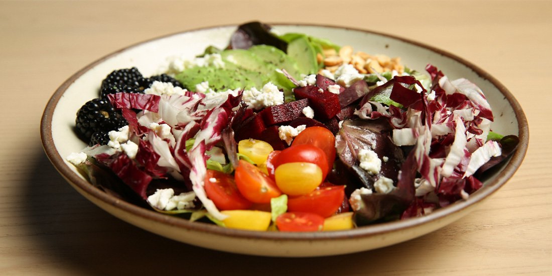 Mixed salad with cherry tomatoes, cucumbers, beets, blackberries, lettuce, and feta cheese in a bowl.
