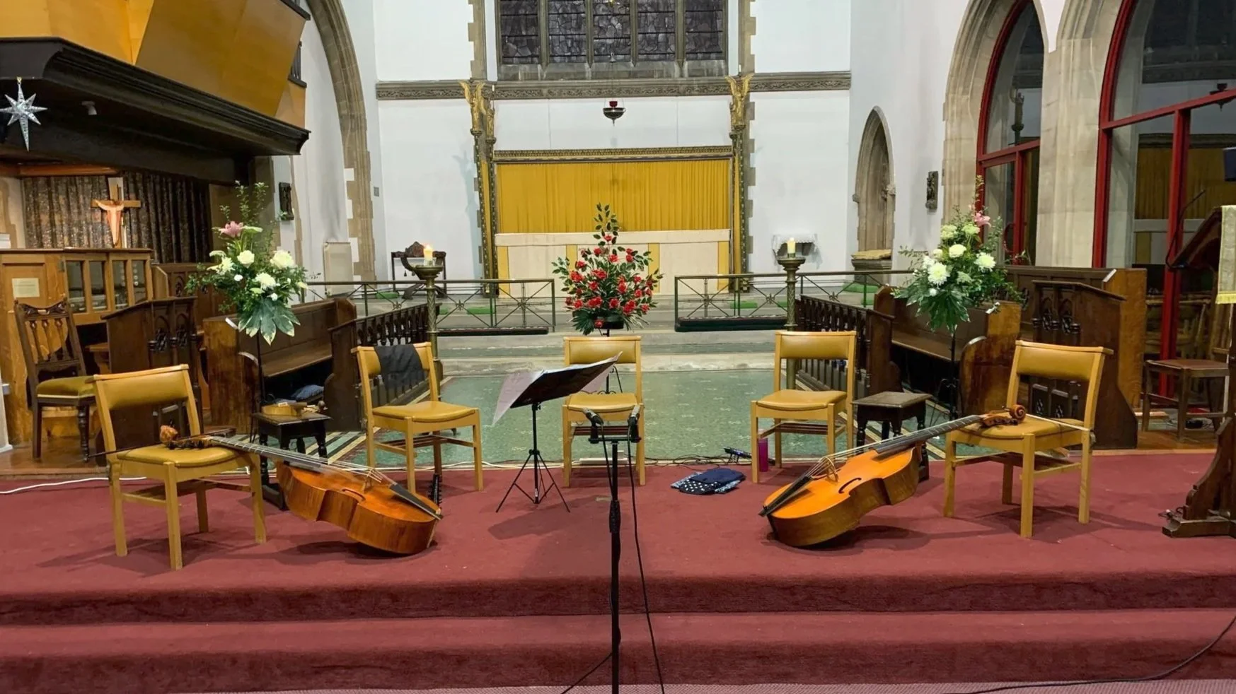 Empty church altar decorated with flowers and candles, musical chairs with guitars, a music stand, and a microphone in front, preparing for a performance or ceremony.