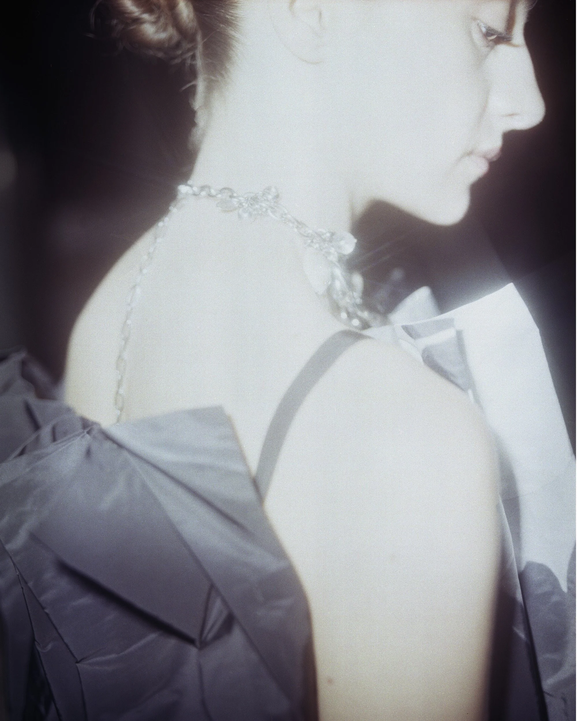 A woman with fair skin and red hair wearing a silver necklace and a light-colored dress with puffed sleeves, captured in profile with her eyes closed.