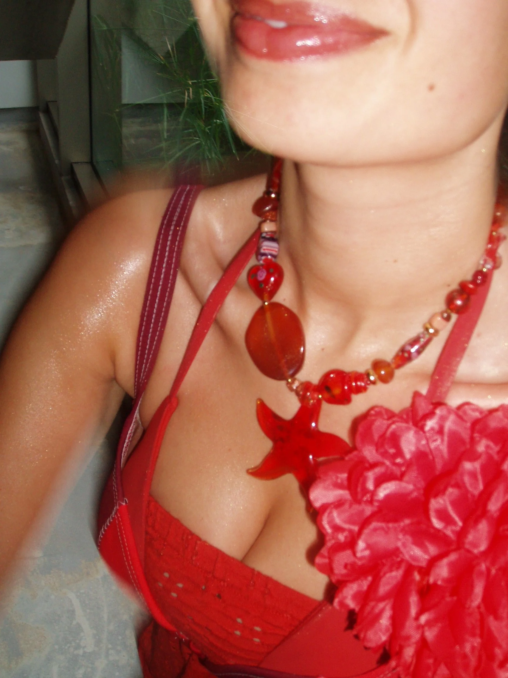 Close-up of a woman's neck and shoulder wearing red jewelry and a red dress with a large pink flower accessory.
