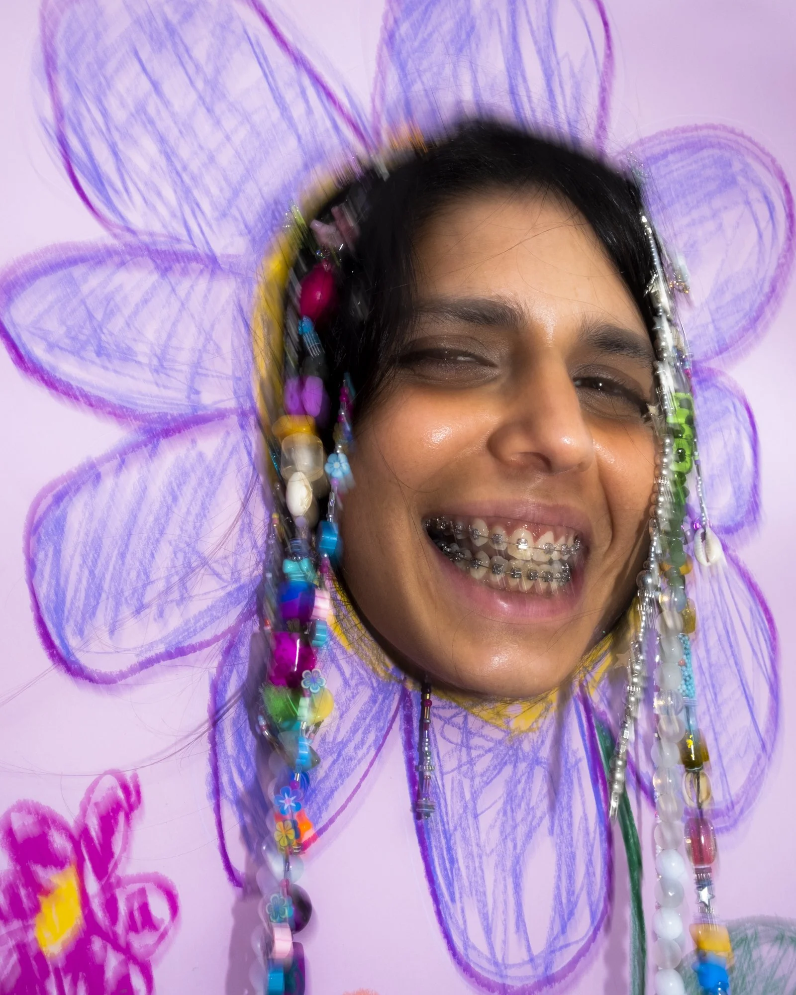 A person smiling with braces, surrounded by a colorful drawing of a flower with purple petals and a pink background, with beads and small toys hanging around their face.