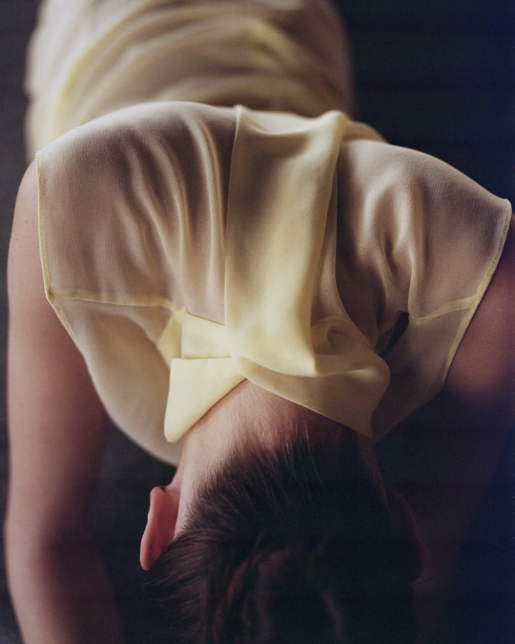 Person lying face down on a dark surface, wearing a beige top, with dark hair covering their face.