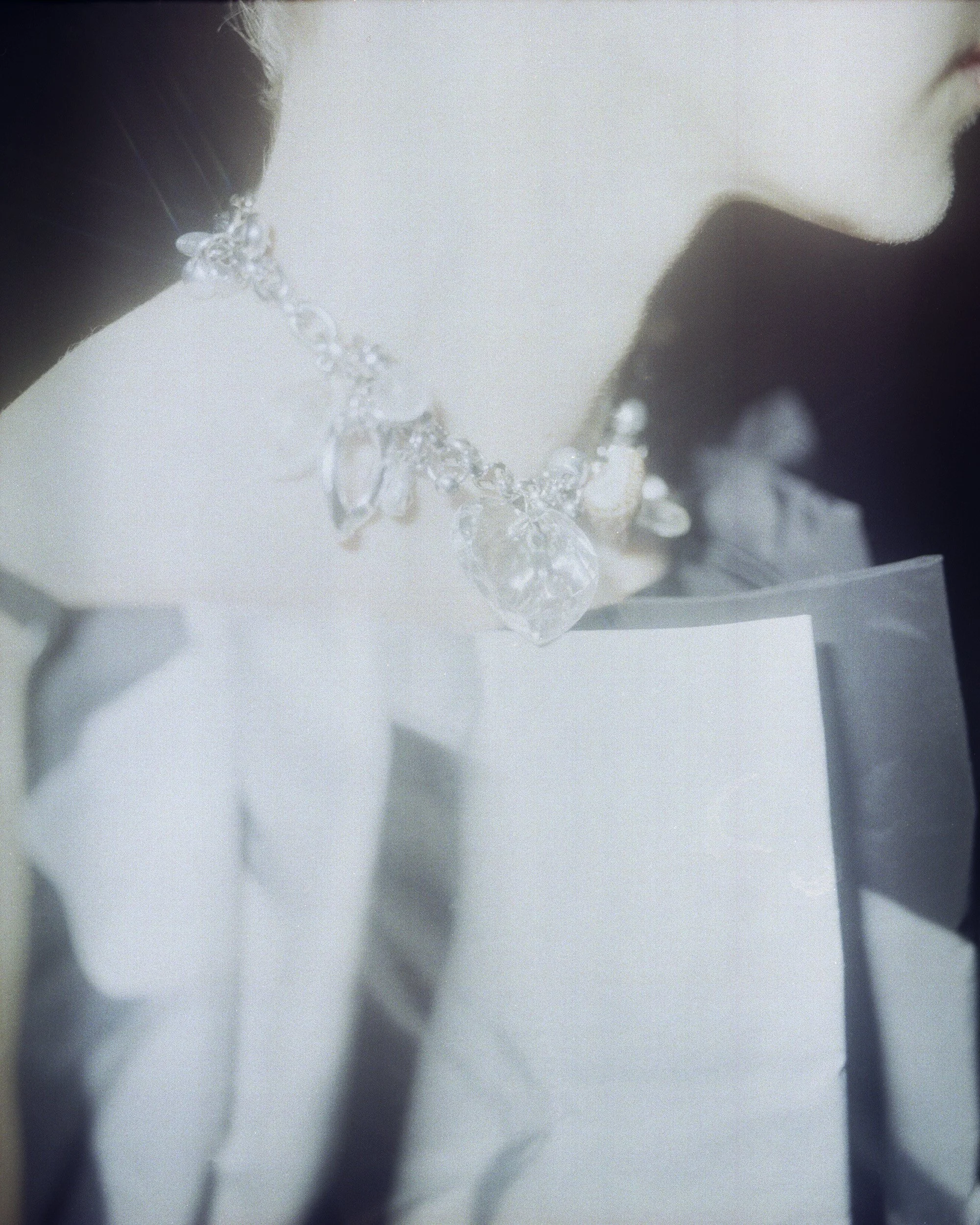 Close-up of a woman wearing a diamond necklace and black jacket, with her face partially visible, reflected in a mirror.