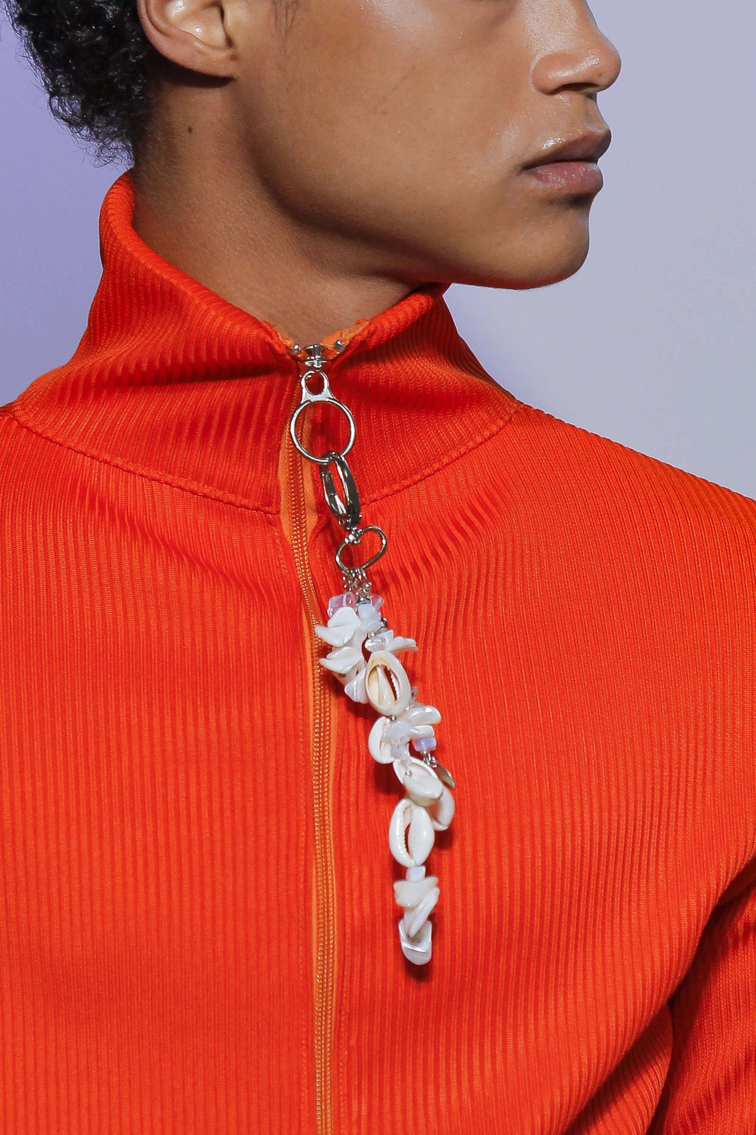 Close-up of a person wearing an orange zip-up jacket with a decorative zipper pull made of white shells