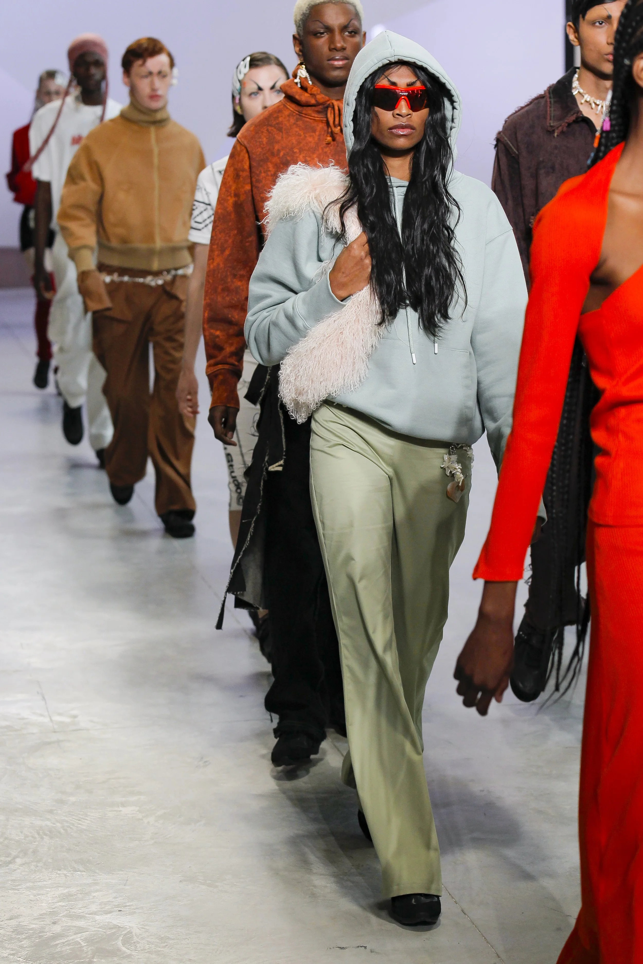A diverse group of models parade down a runway during a fashion show, showcasing various stylish outfits.