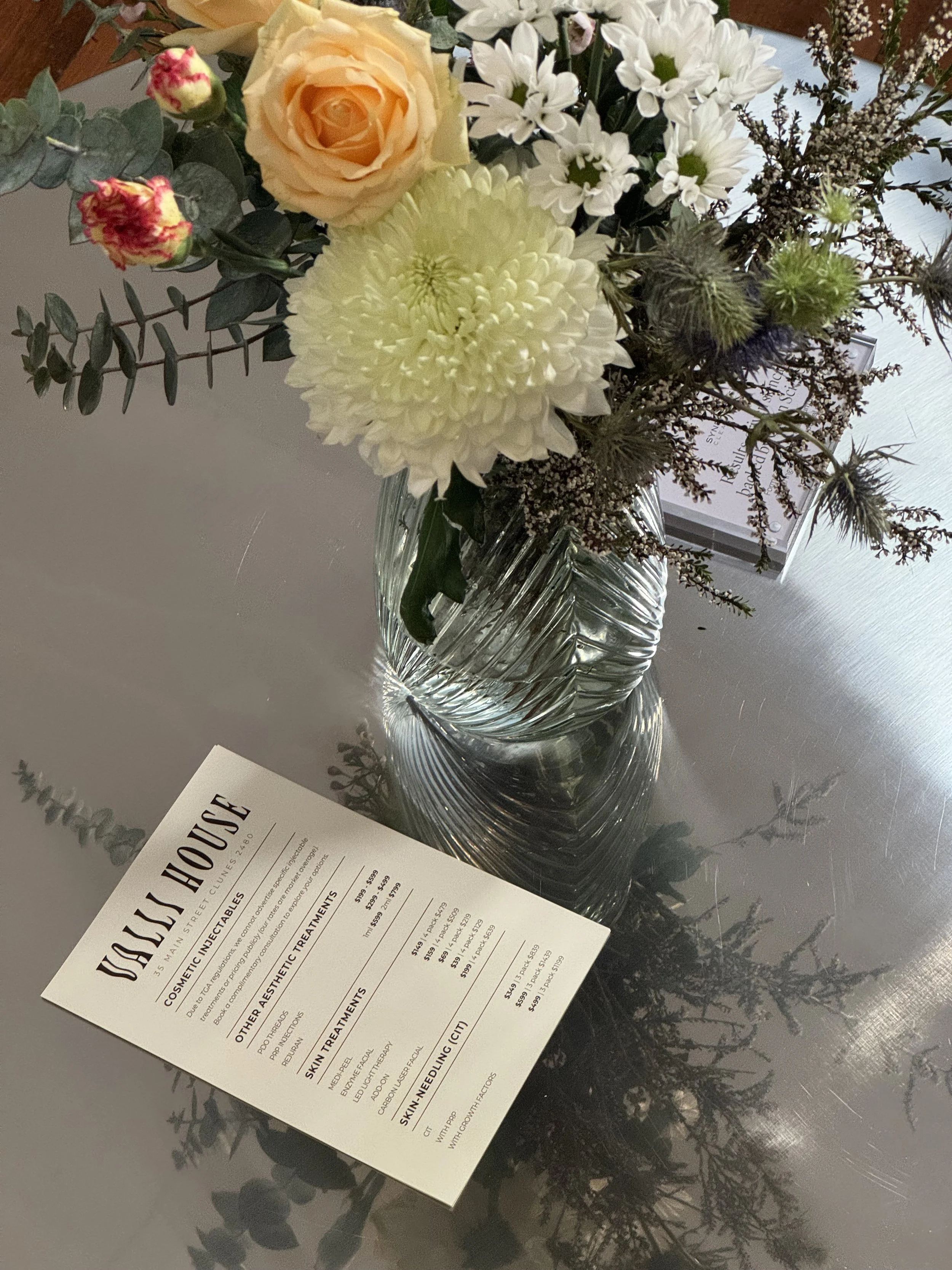 treatment menu for injectables and skin treatment on silver table with bunch of flowers
