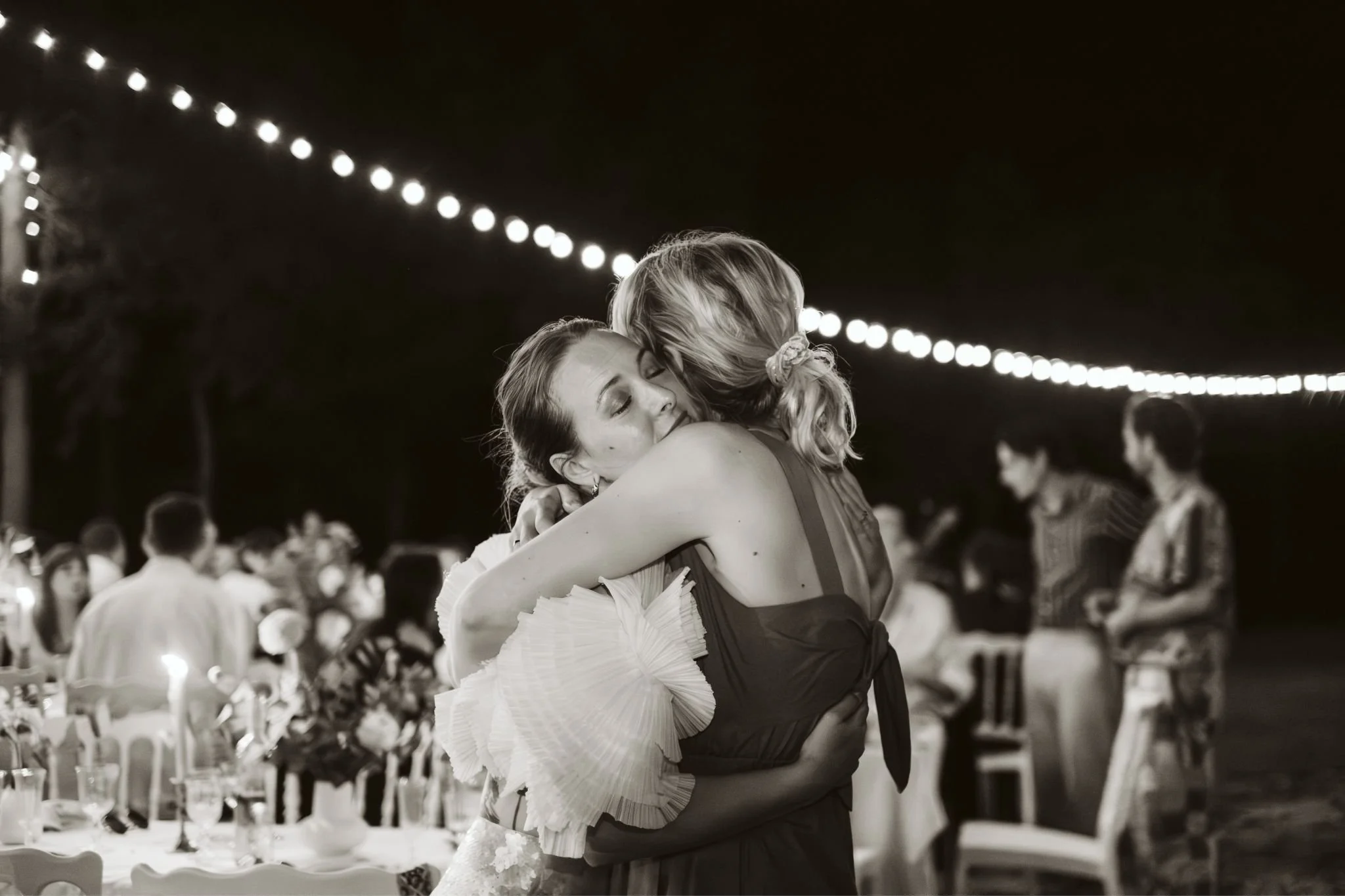 Mariée serrant sa sœur dans ses bras pendant le dîner de mariage en extérieur en Normandie, ambiance intime et chaleureuse.
