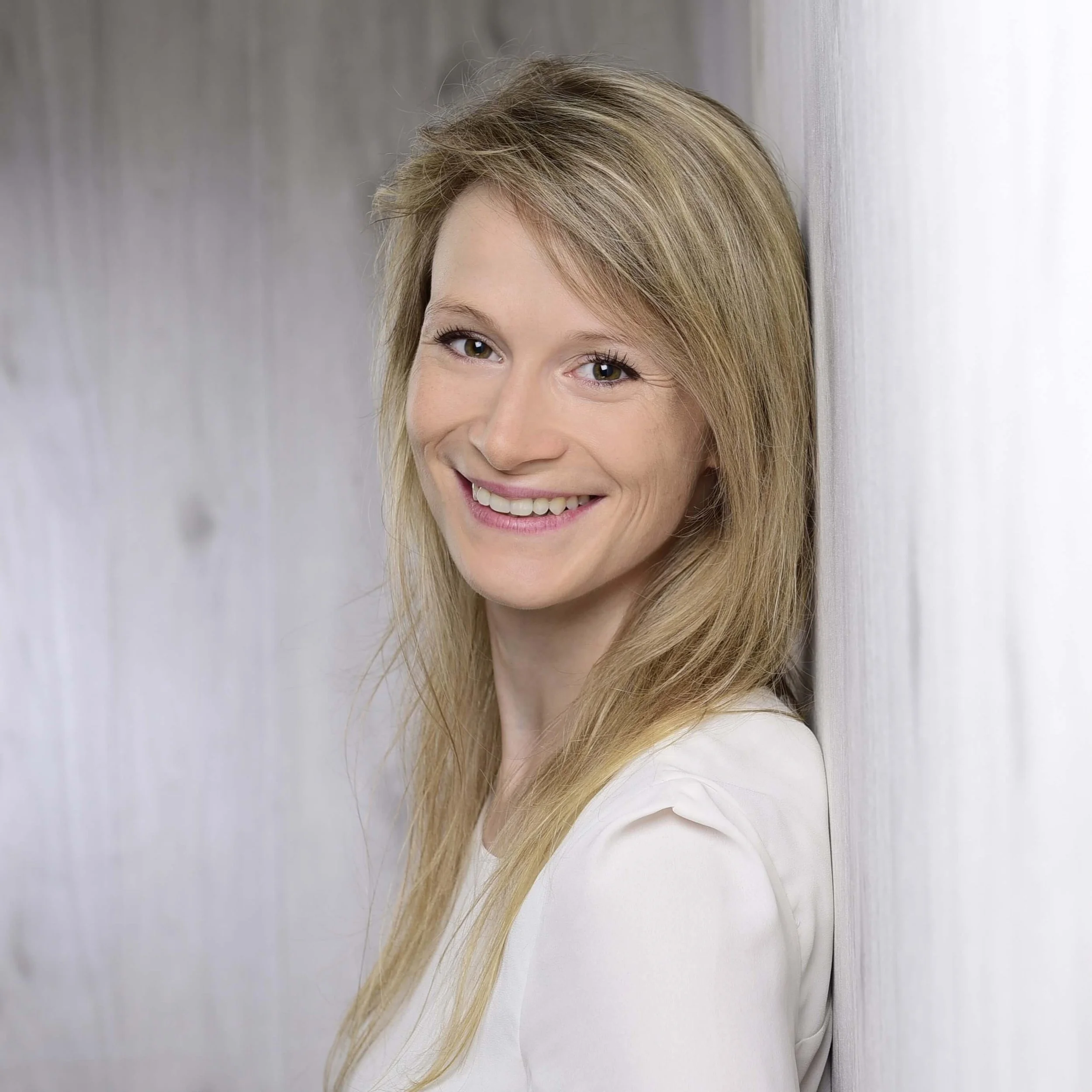 Eine Frau mit langen blonden Haaren steht an einer Wand gelehnt.