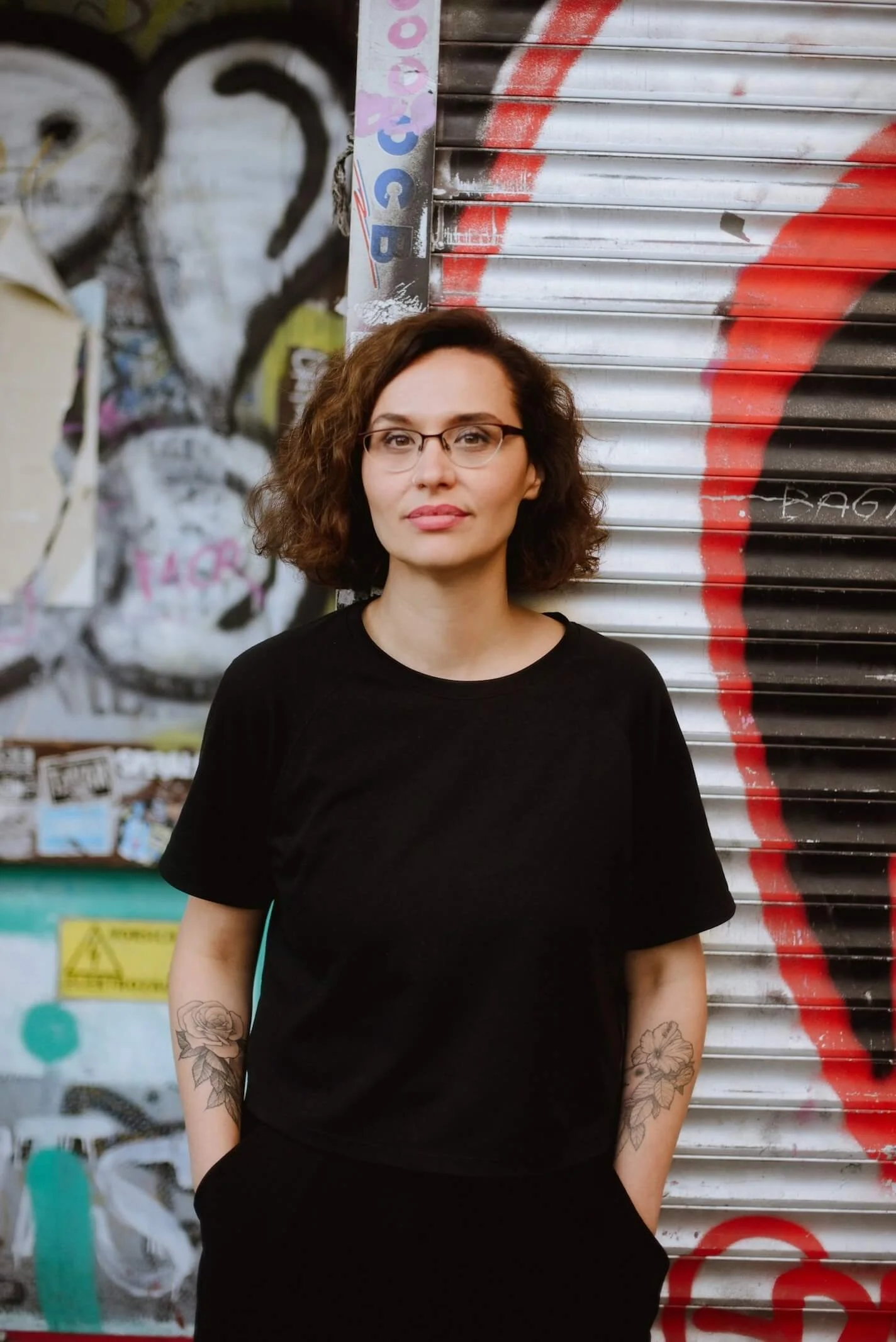 Porträt von Canan Turan vor einer Wand mit Graffiti, ihre Tattoos sind sichtbar.