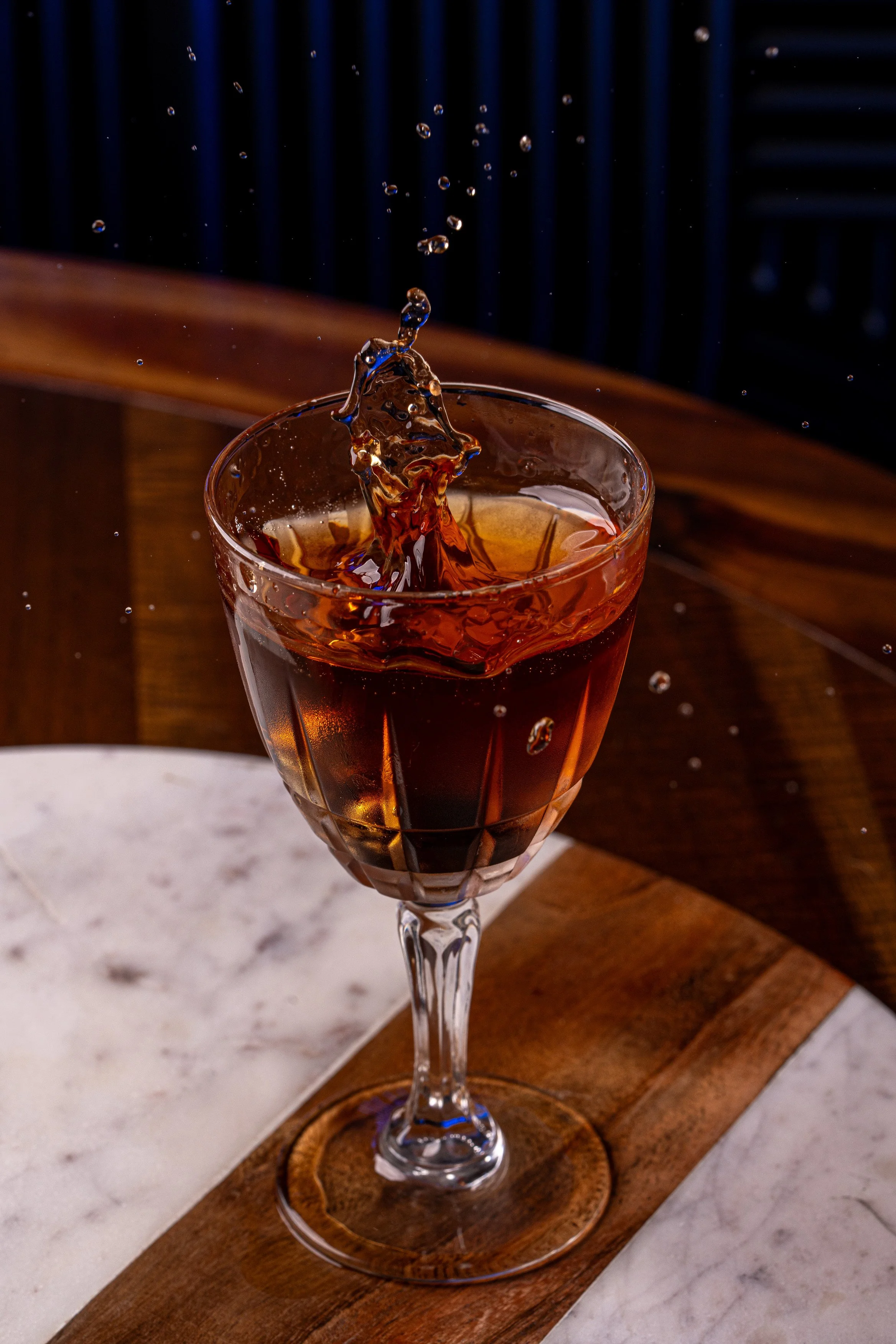 A splash of liquid in a glass on a marble and wooden table.