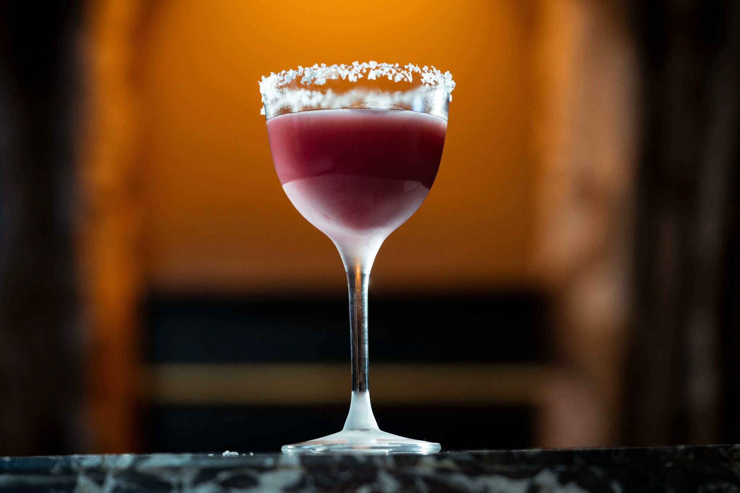 Cocktail glass with red drink and salt rim on dark background