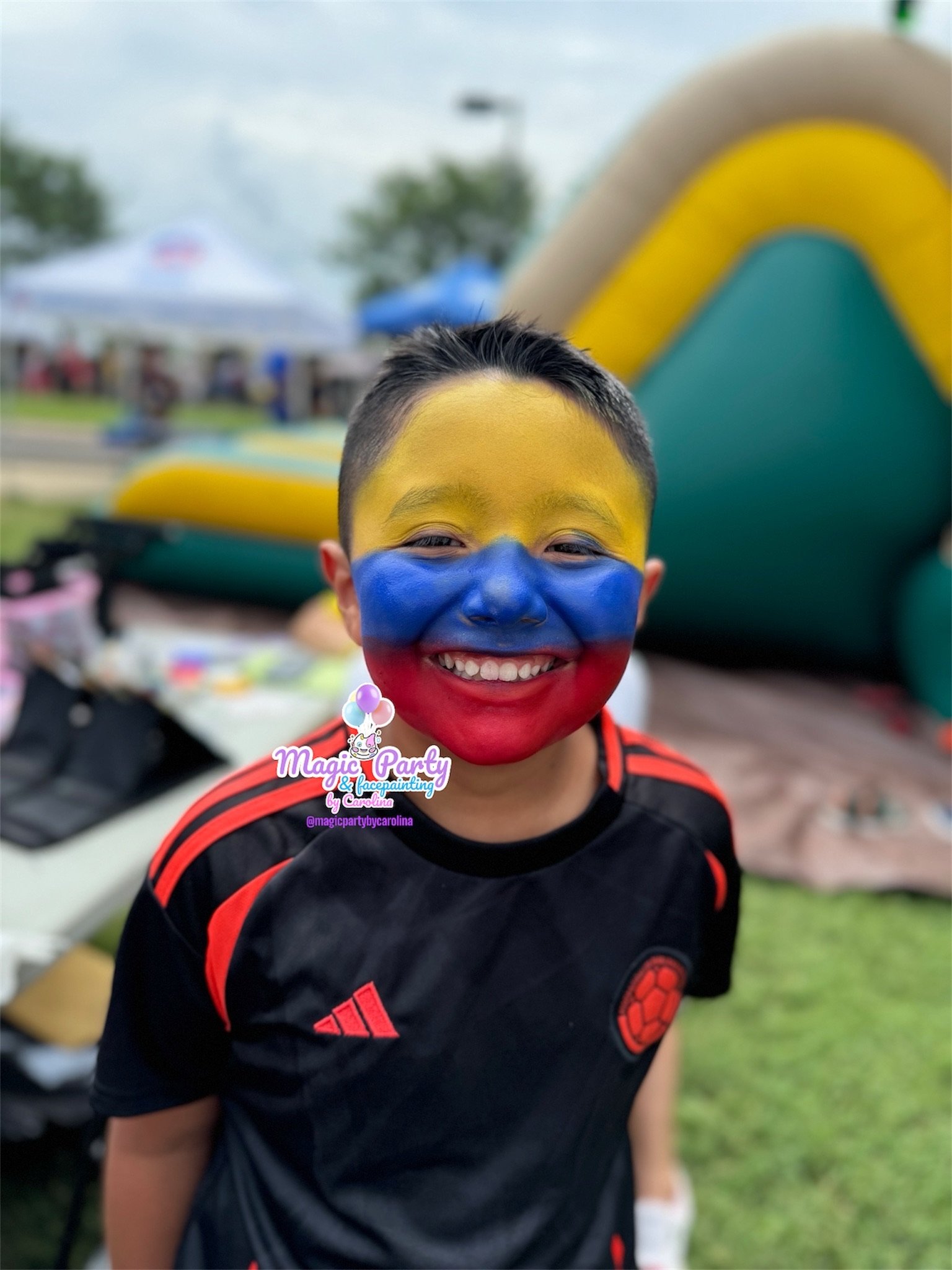 Child with Colombian flag face paint smiling at an outdoor event.