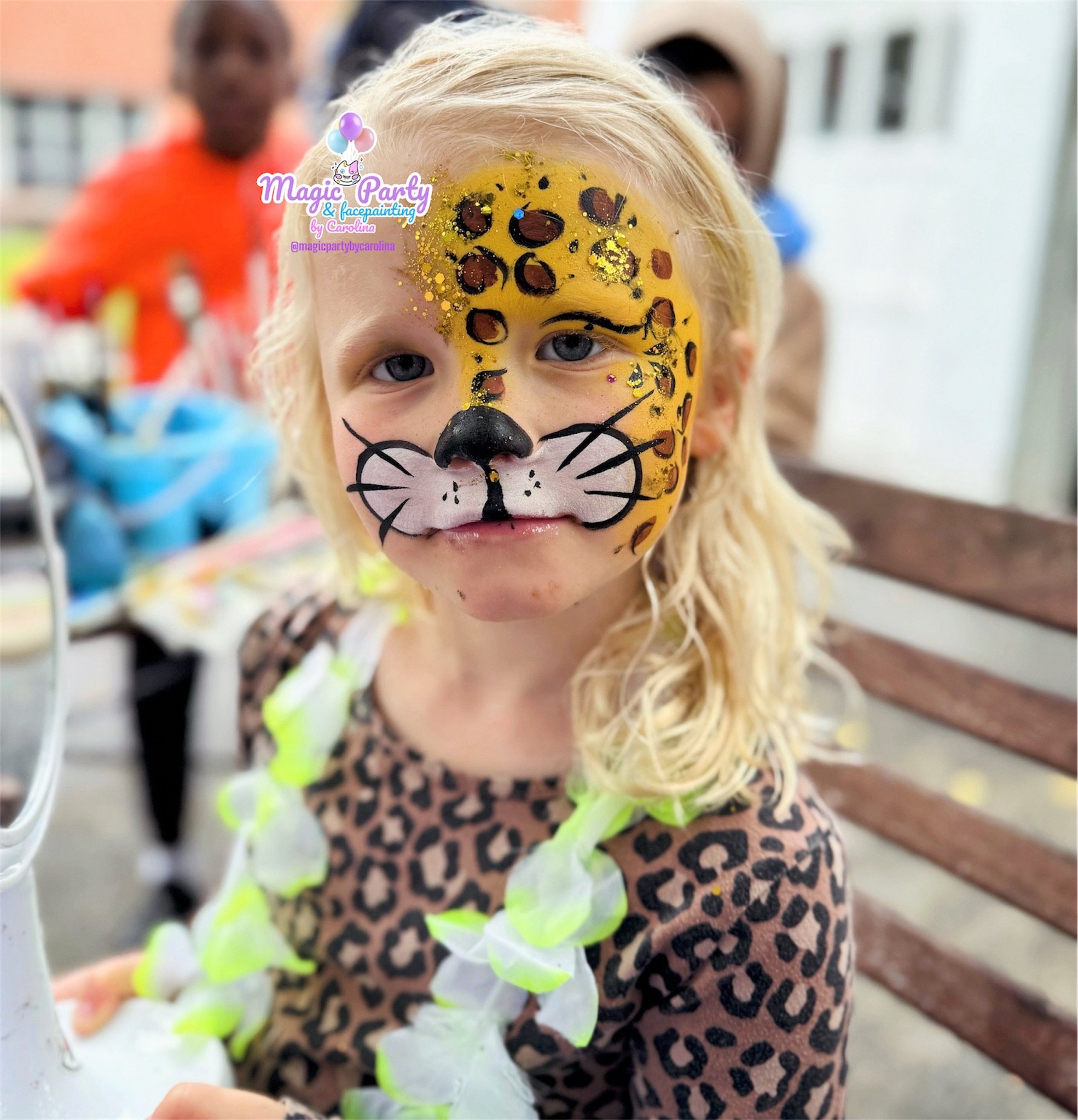 Child with leopard face paint and patterned shirt, wearing a green and white lei