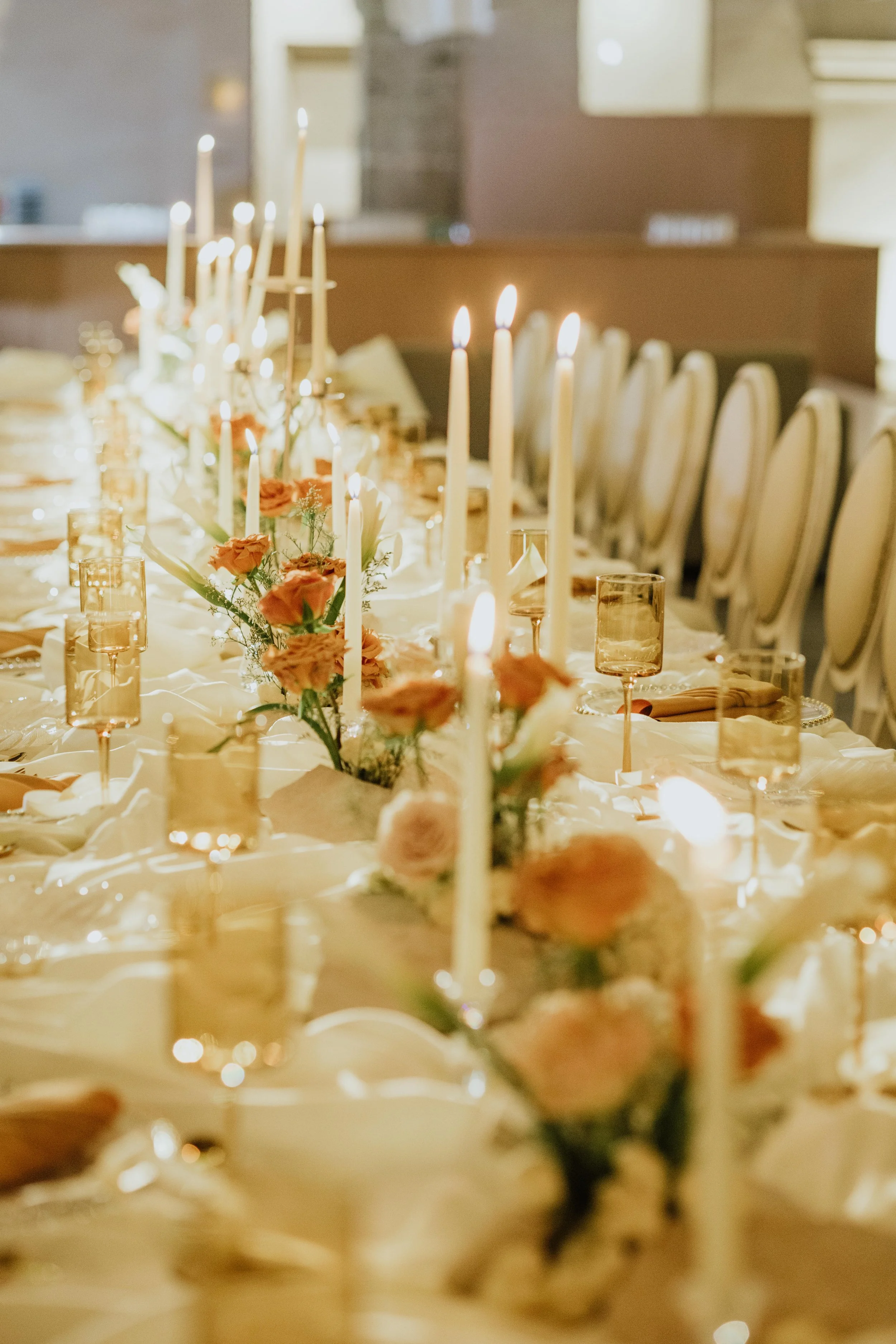 Mesa decorada con velas, flores rosadas y cristalería en un evento formal.