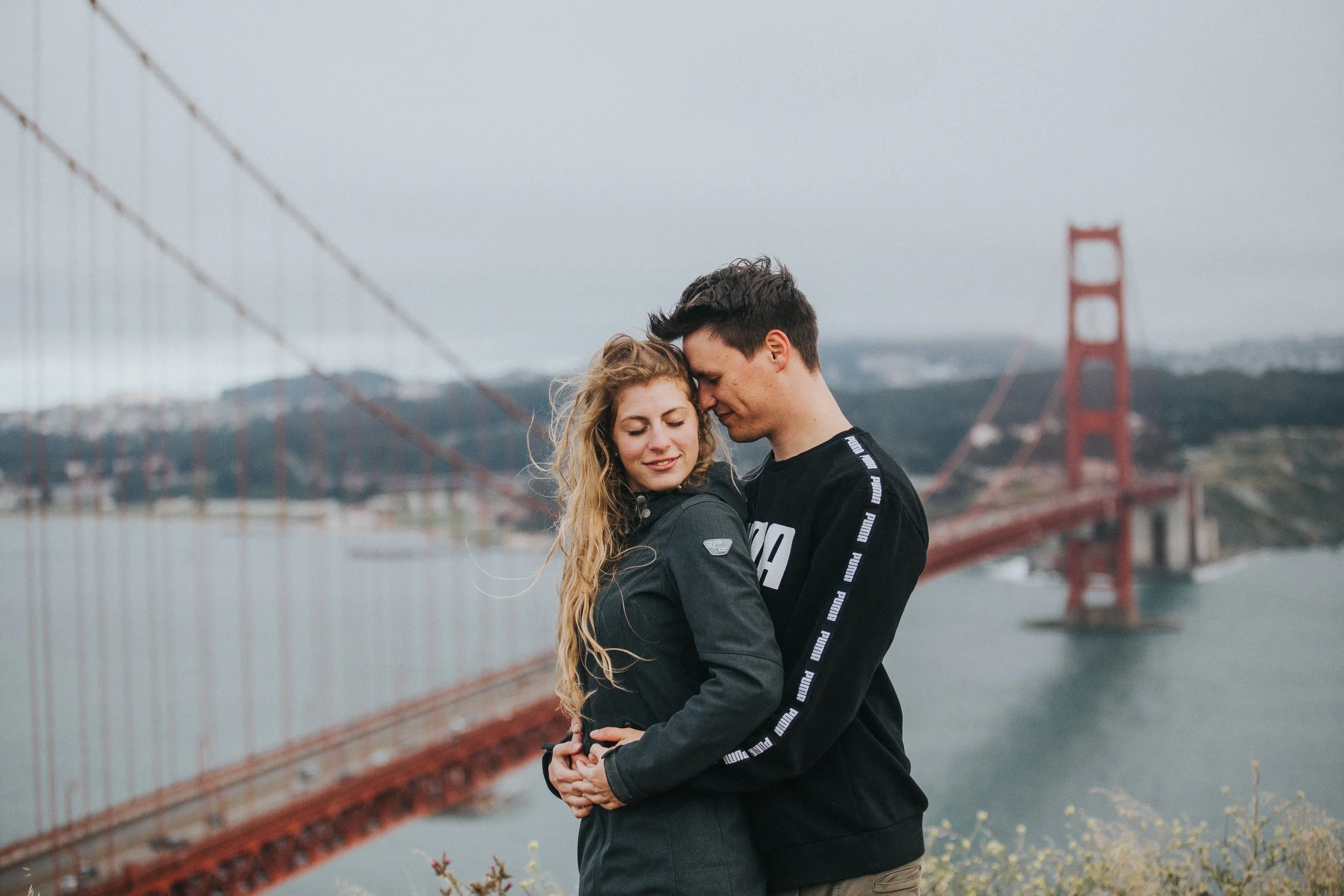 Joven pareja abrazándose frente al puente Golden Gate en San Francisco, California.