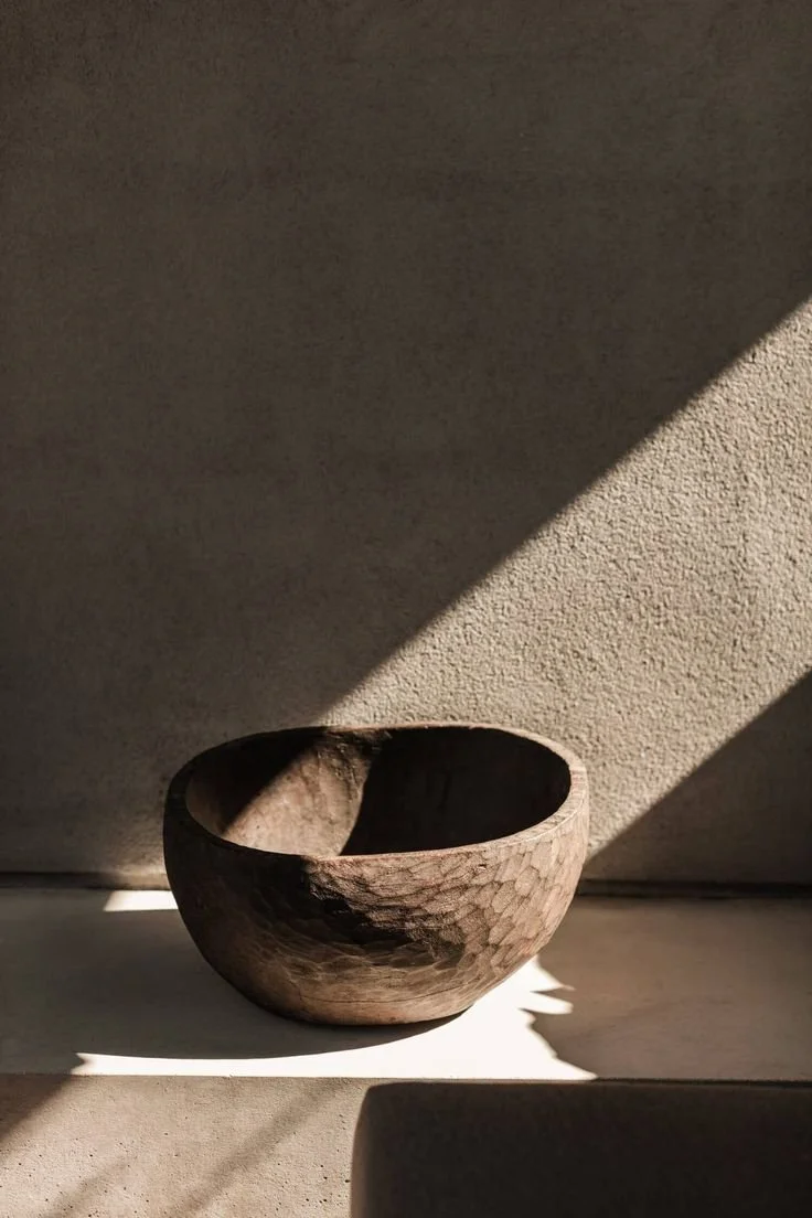 A wooden bowl on a surface, casting shadows in sunlight.