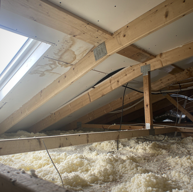 Wooden beams and metal brackets above white insulation material in an attic with a skylight.