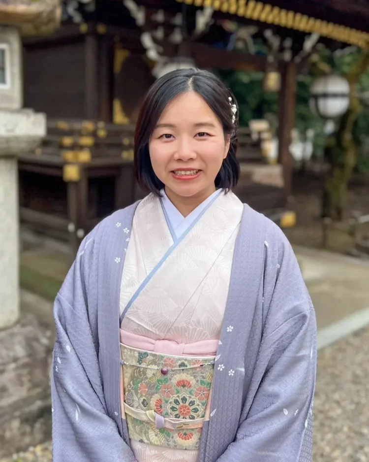 A young woman dressed in traditional Japanese kimono standing outdoors near a shrine or temple.